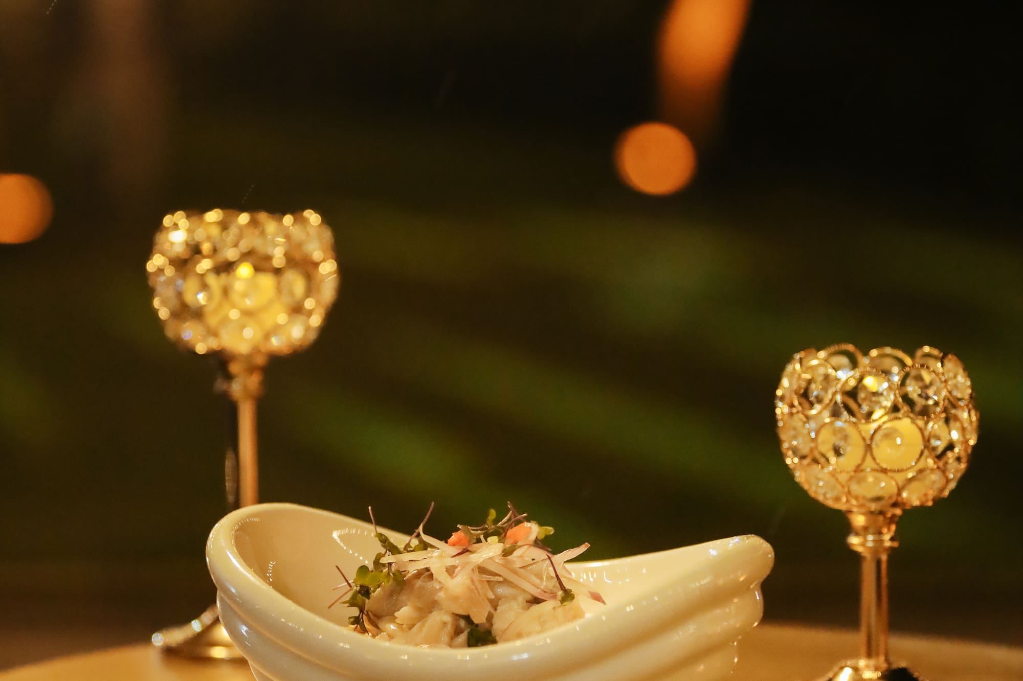 Plato de ceviche en mesa con copas doradas, luces bokeh nocturnas.