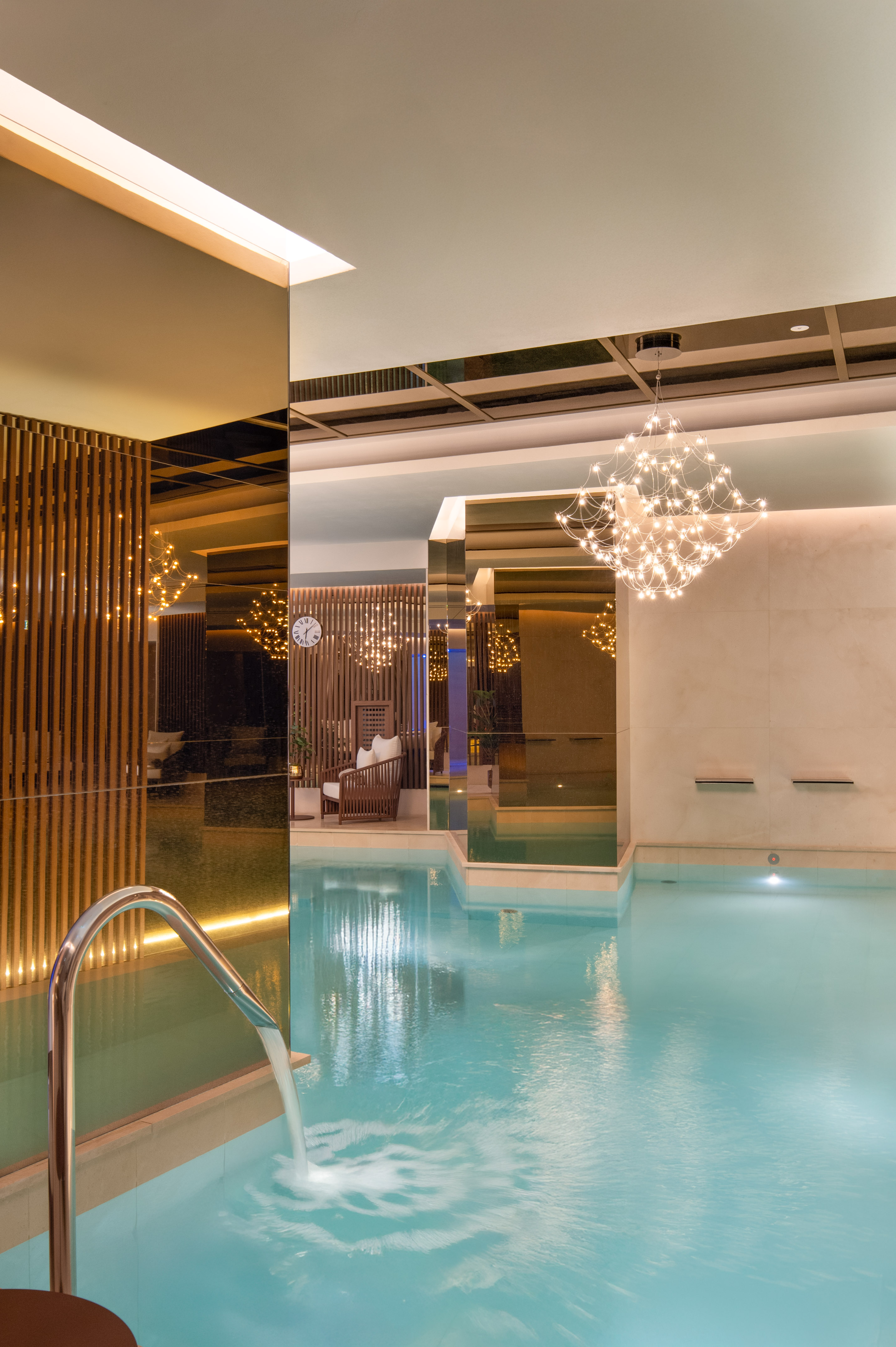 Modern indoor spa pool with water cascade, mirrored interior, and ambient lighting.