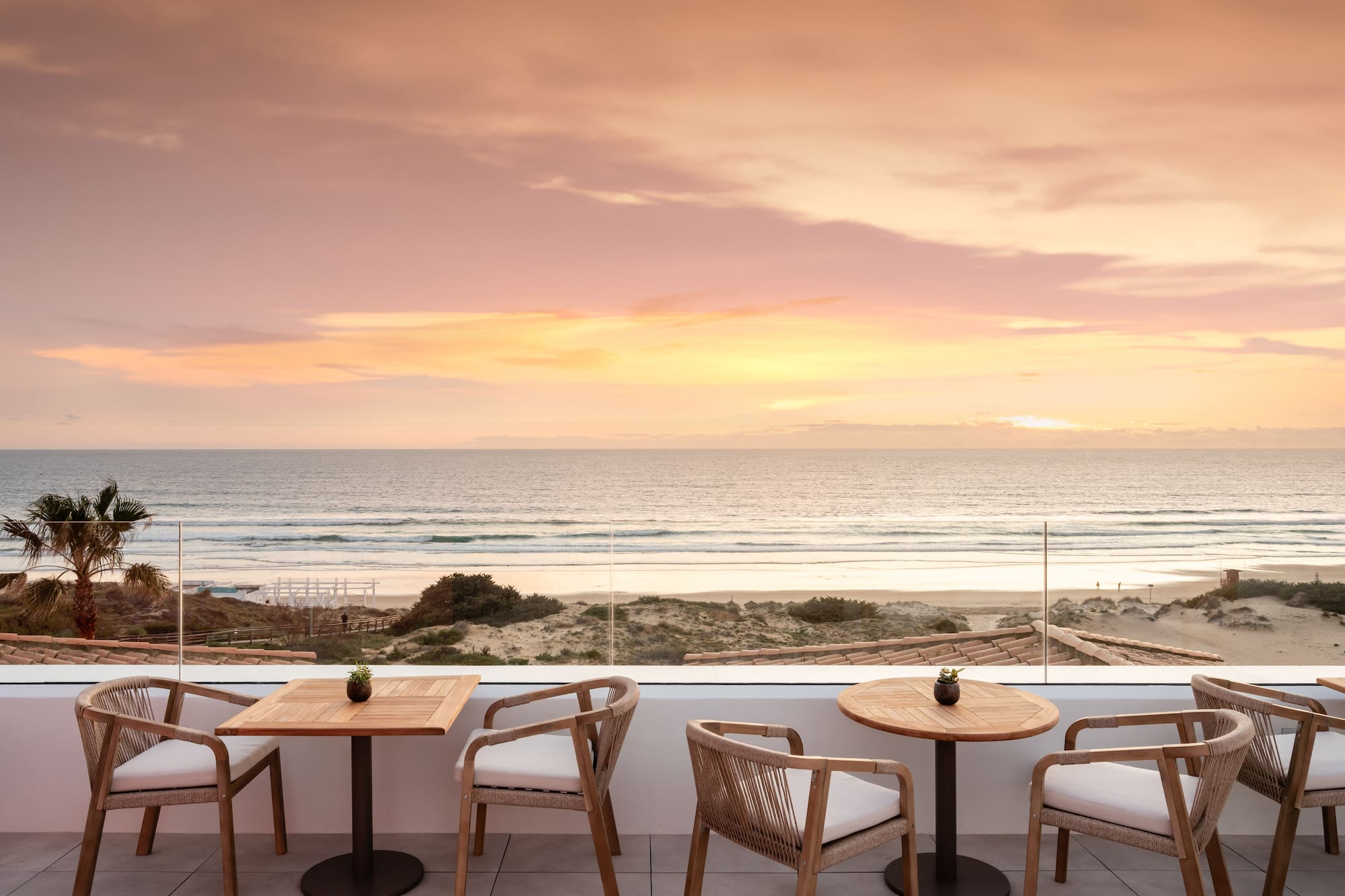 Sunset ocean view from hotel terrace with beach and outdoor seating.