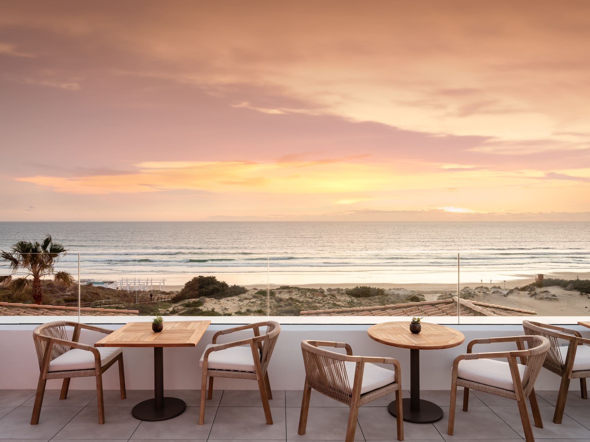 Sunset ocean view from hotel terrace with beach and outdoor seating.