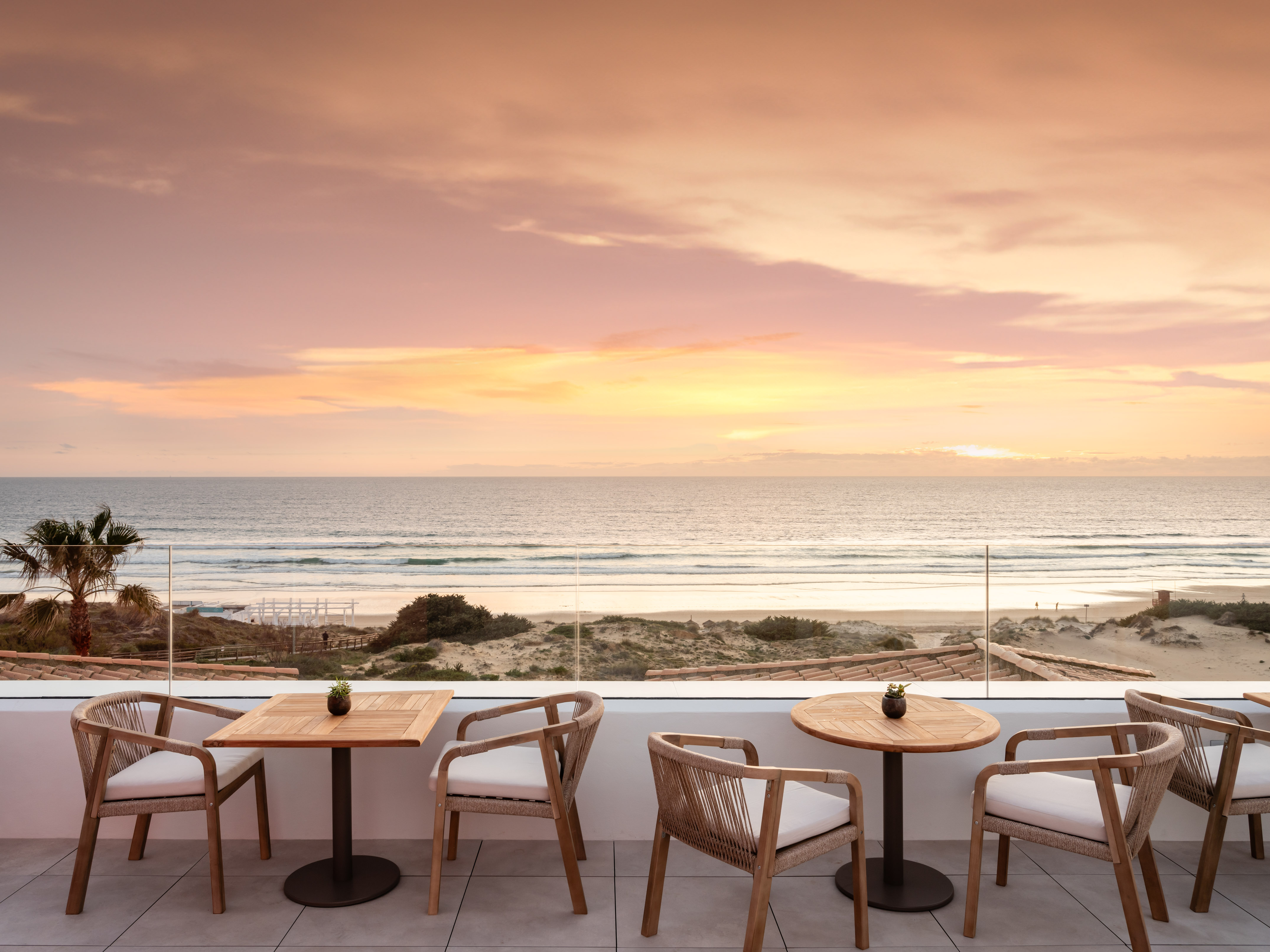 Sunset ocean view from hotel terrace with beach and outdoor seating.