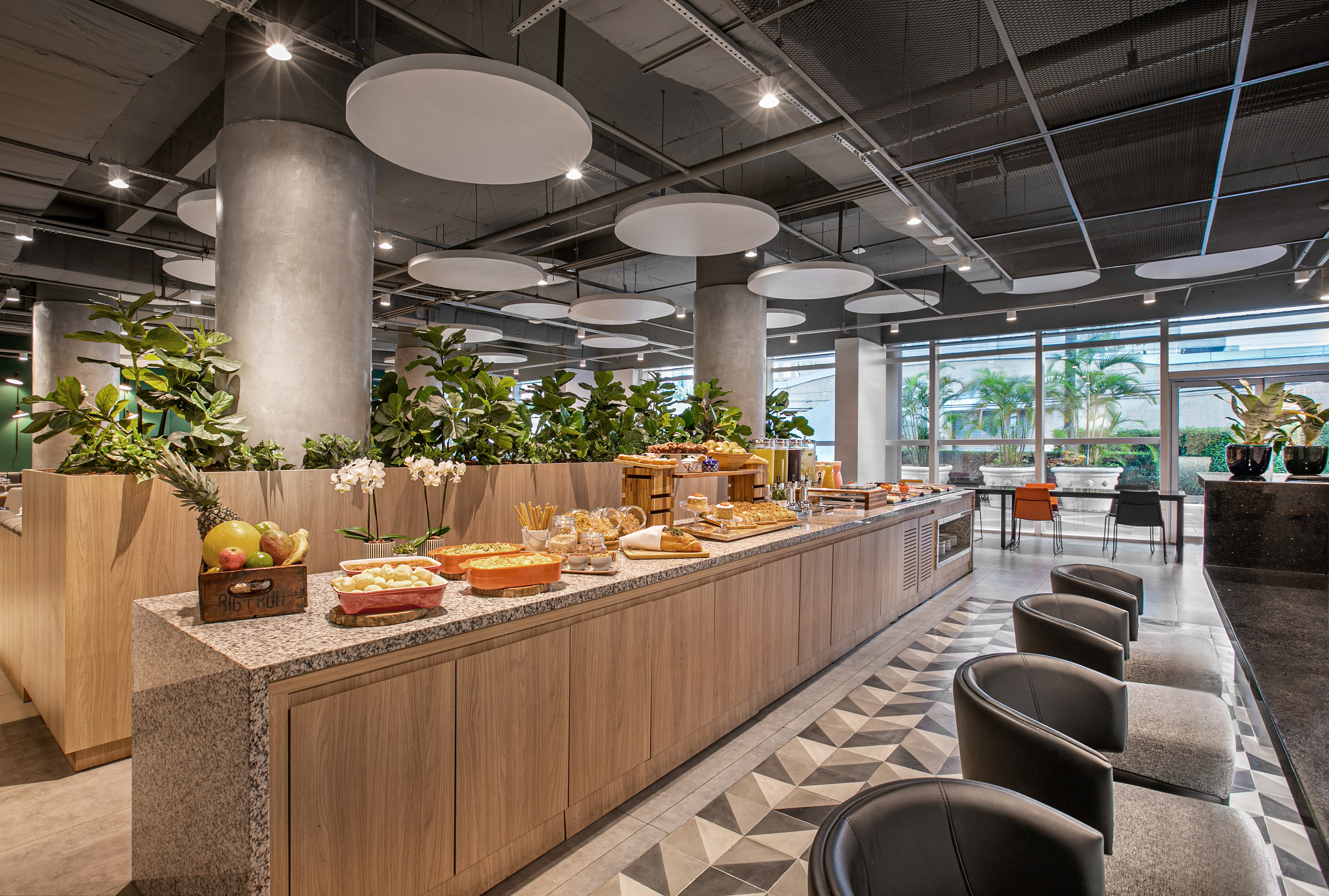 Modern hotel breakfast buffet with fresh food, fruit, and plants.