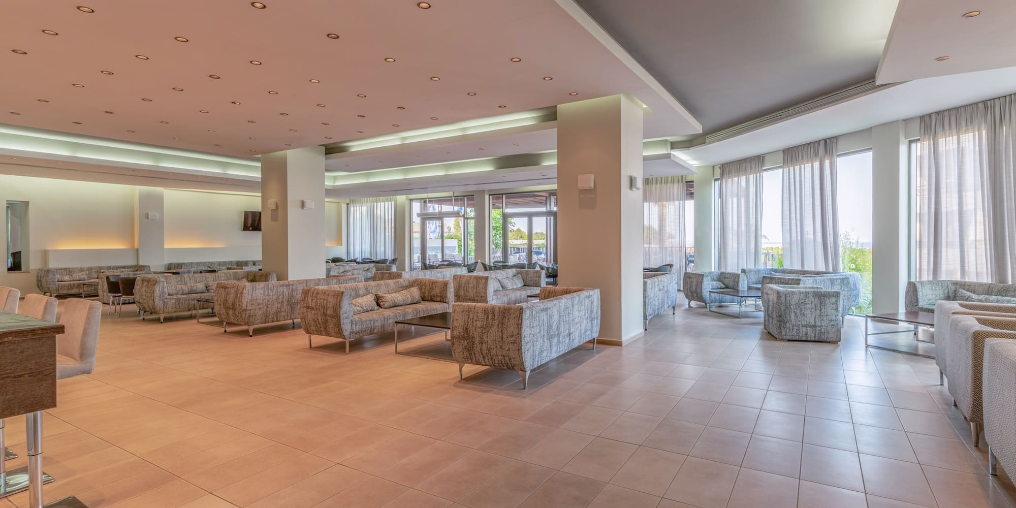 Modern hotel lobby lounge with comfortable sofas, tiled floor, and bright windows.