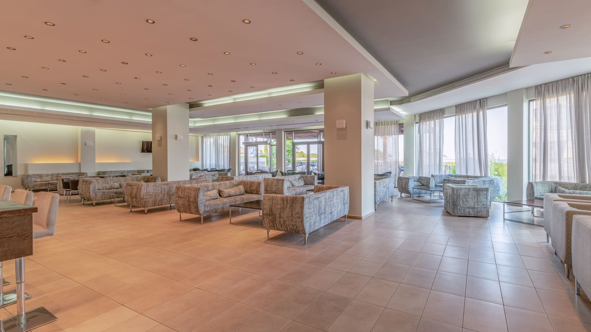 Modern hotel lobby lounge with comfortable sofas, tiled floor, and bright windows.