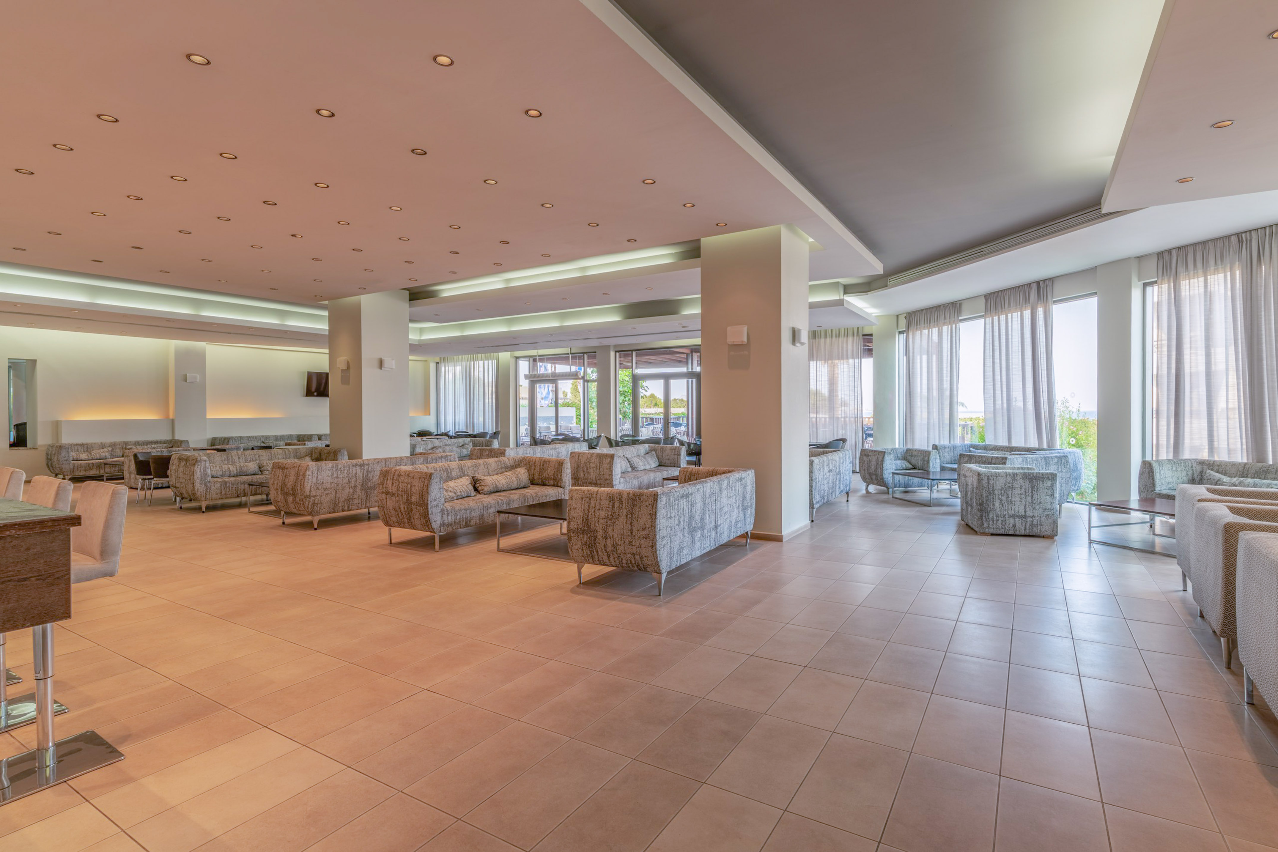 Modern hotel lobby lounge with comfortable sofas, tiled floor, and bright windows.