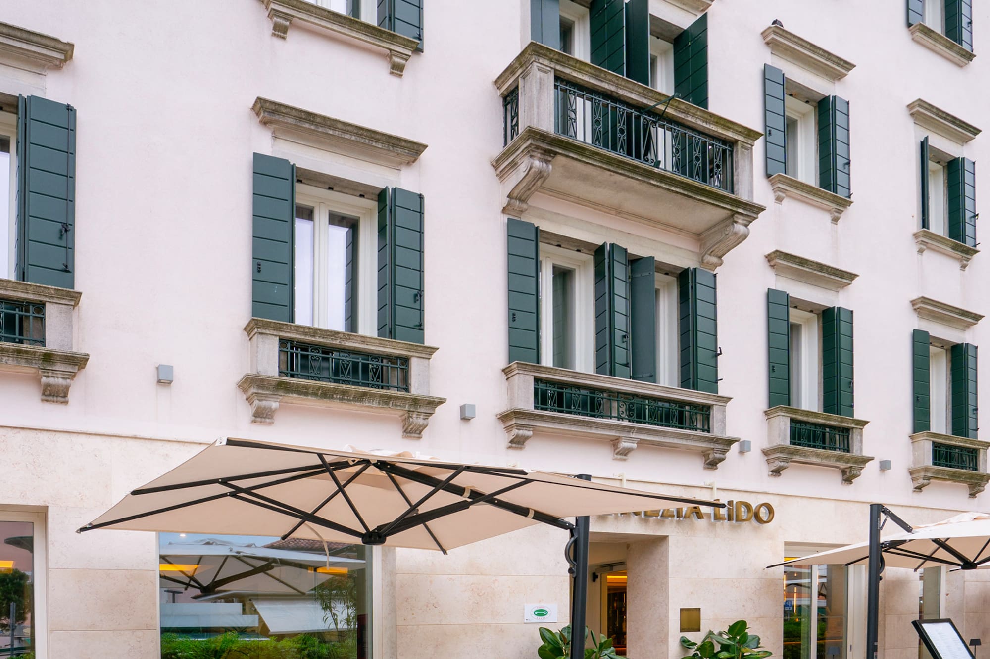 Mellia Hotel Venezia Lido with outdoor patio dining, cream facade, green shutters.