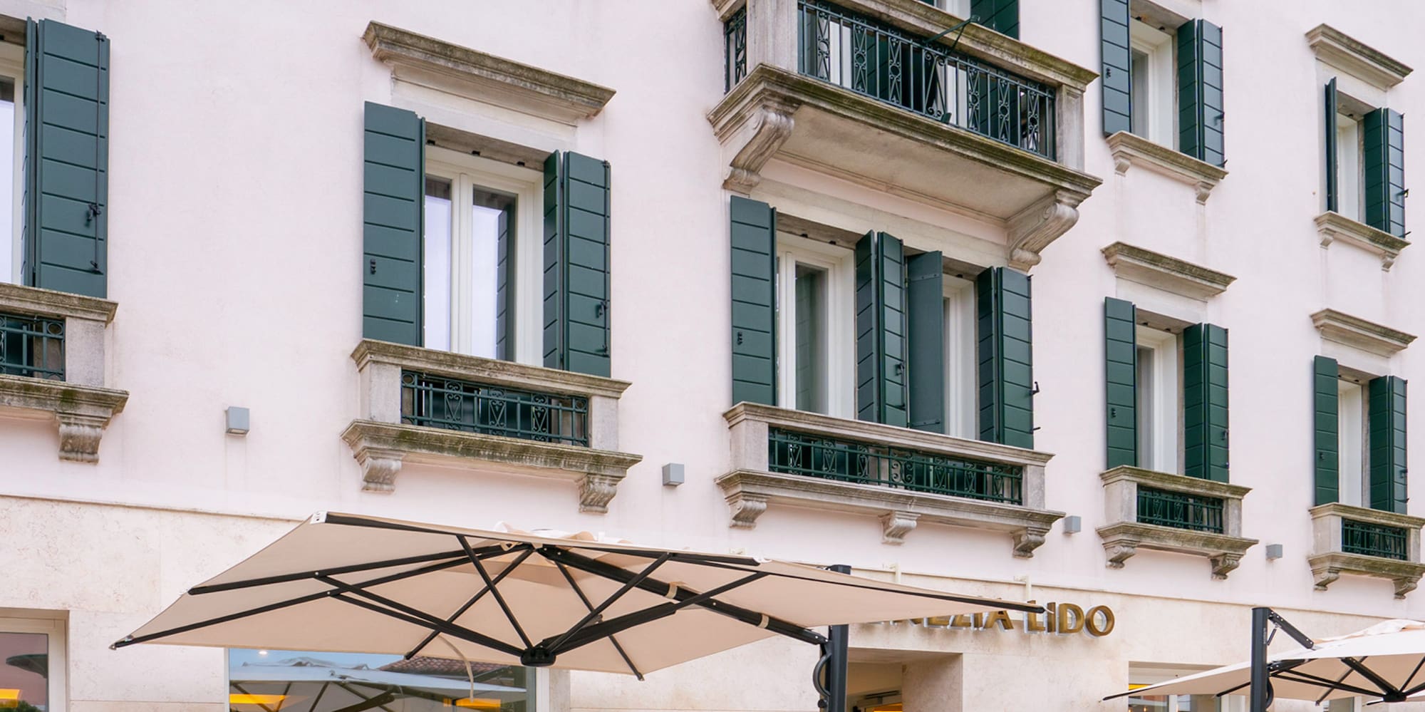 Mellia Hotel Venezia Lido with outdoor patio dining, cream facade, green shutters.