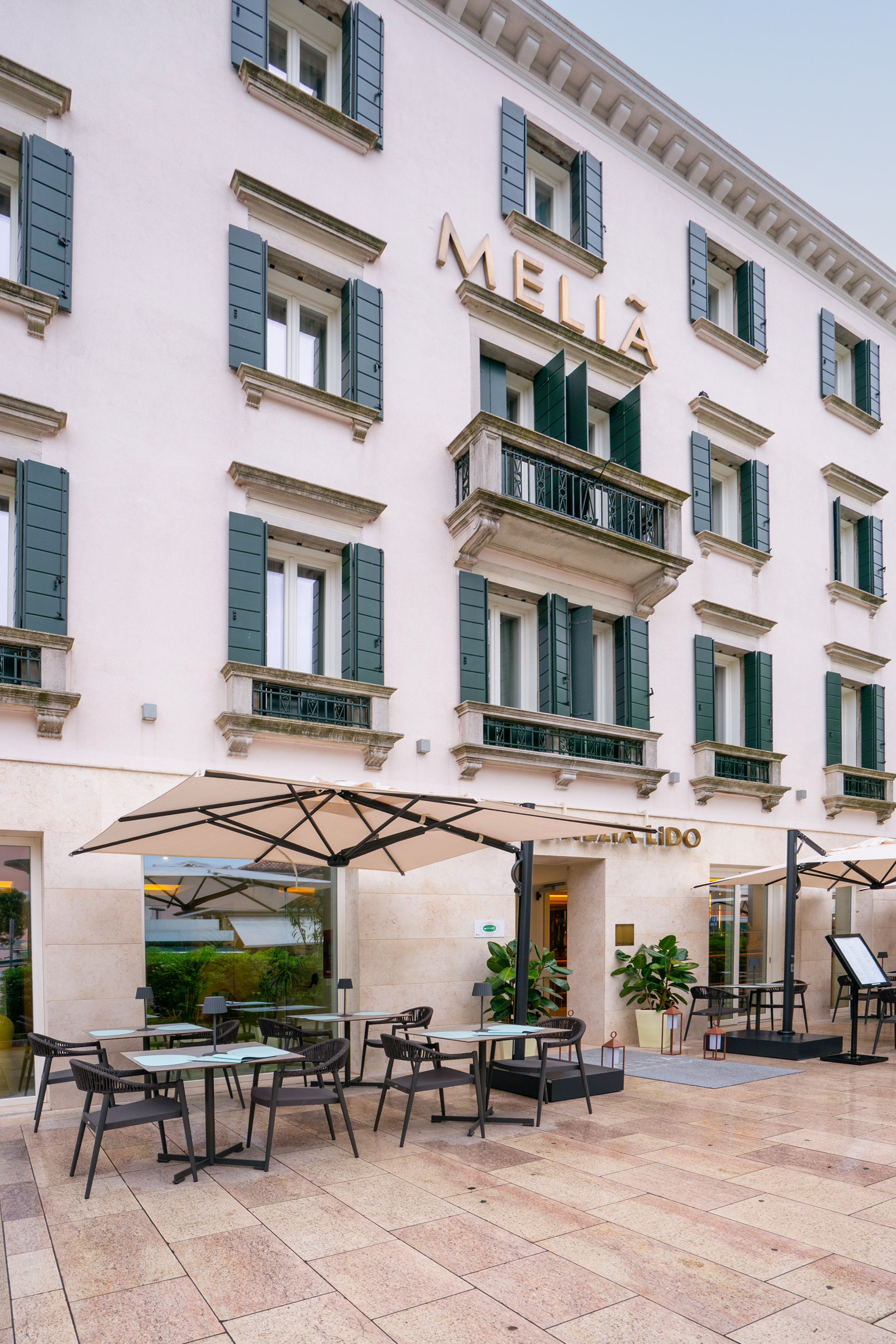 Mellia Hotel Venezia Lido with outdoor patio dining, cream facade, green shutters.
