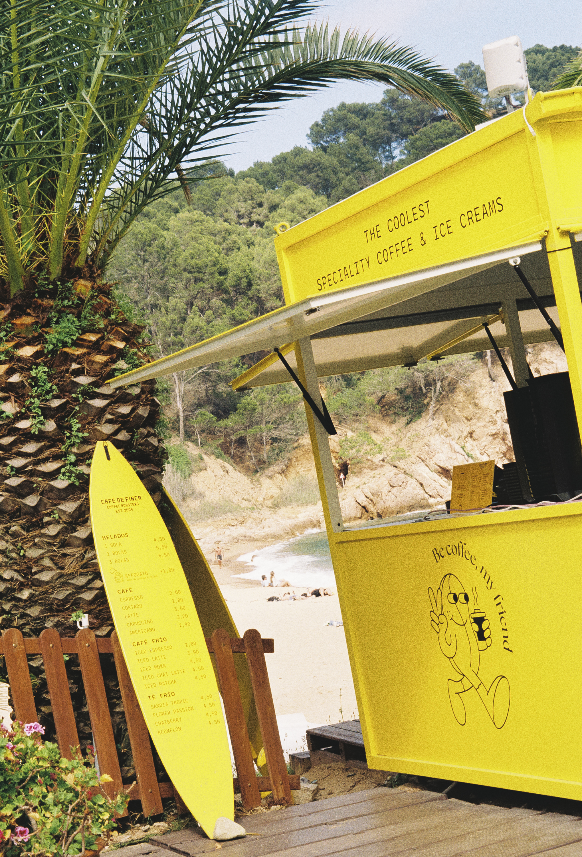 Yellow beach coffee & ice cream stand, surfboard menu, by palm tree.