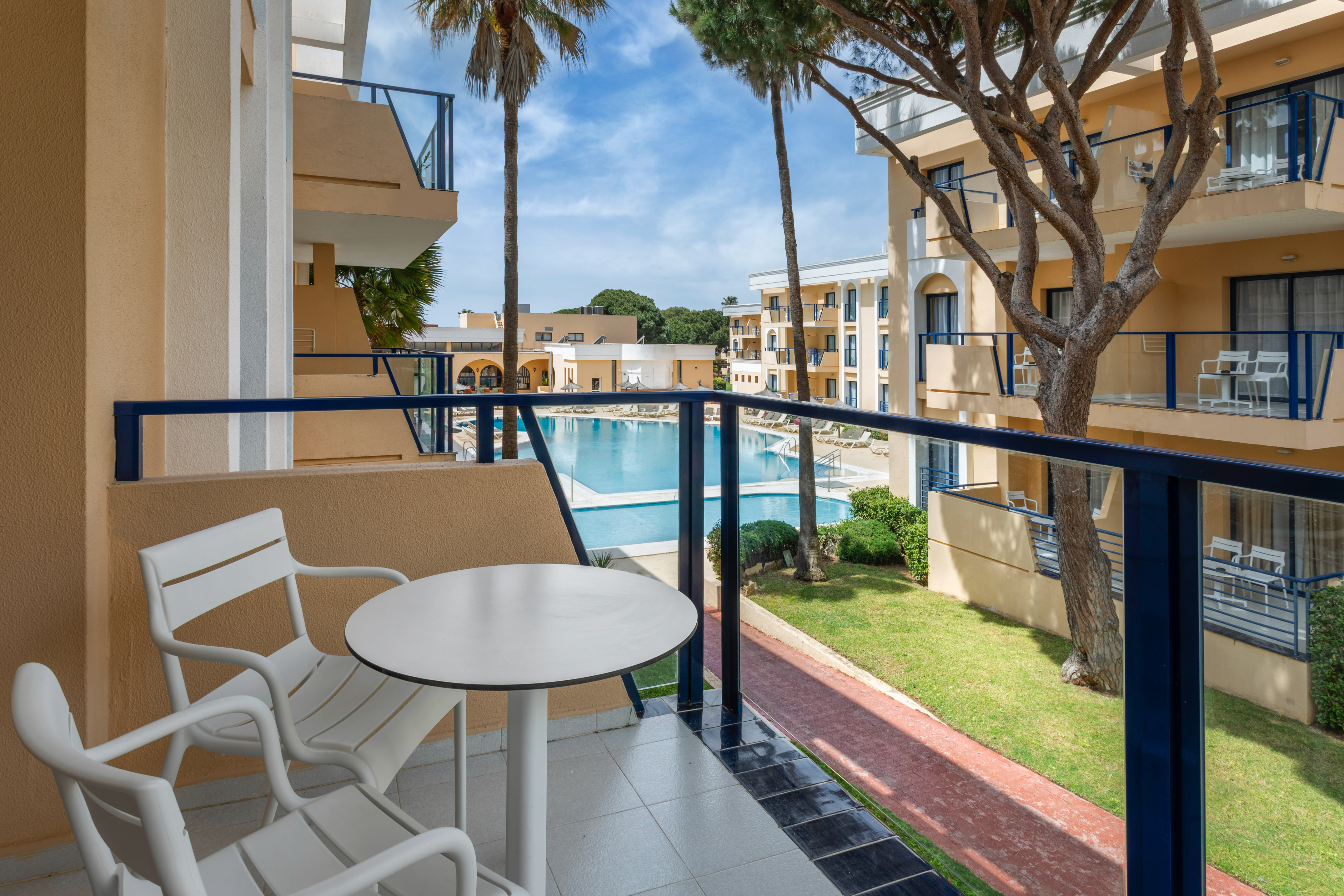 Resort balcony with pool view, white outdoor furniture, and palm trees.