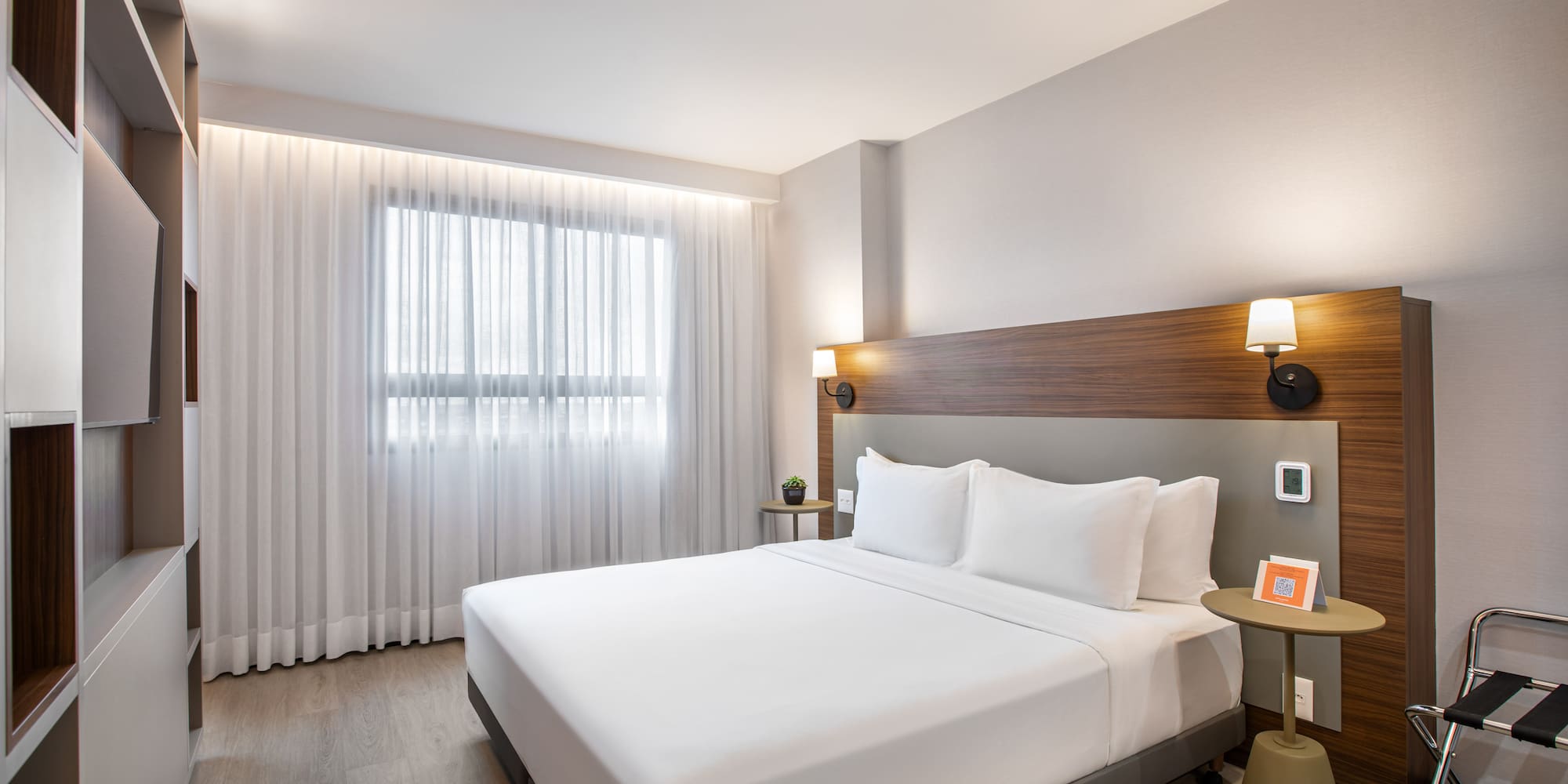 Modern hotel room with king bed, wood headboard, and large window.