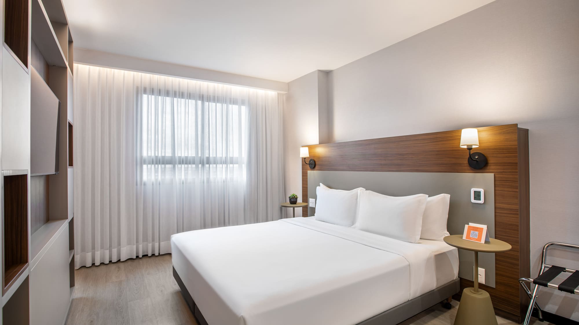 Modern hotel room with king bed, wood headboard, and large window.