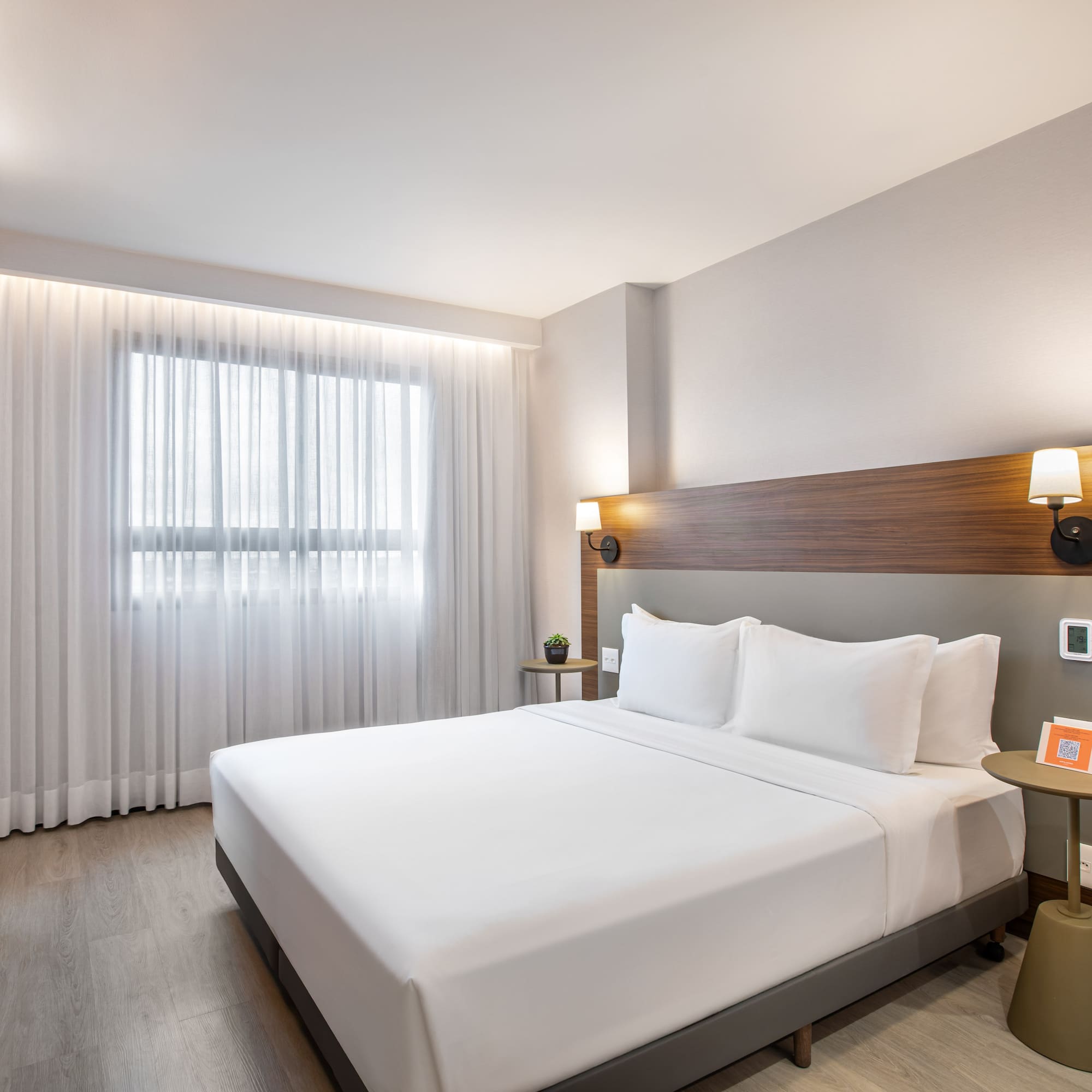 Modern hotel room with king bed, wood headboard, and large window.
