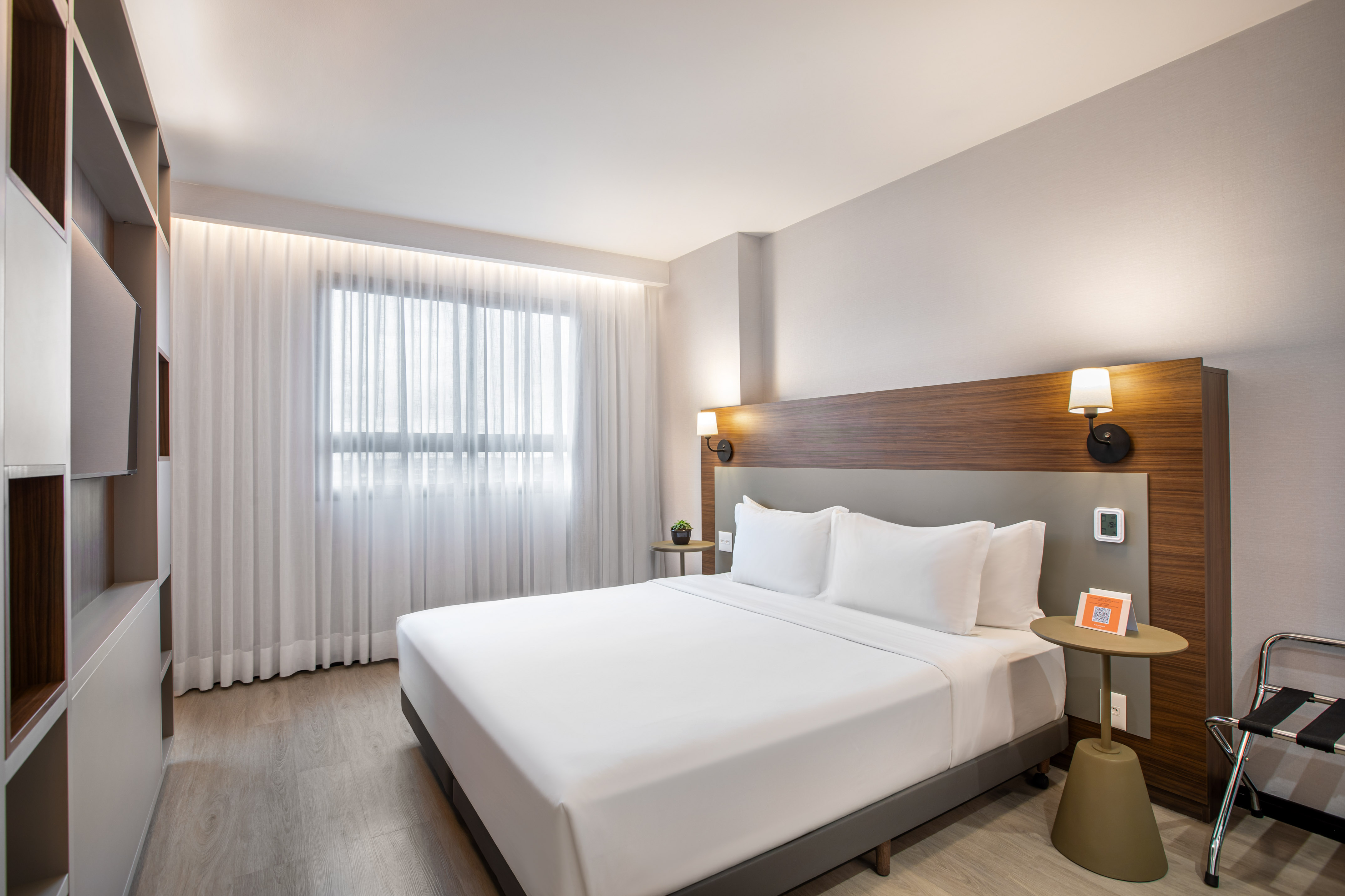 Modern hotel room with king bed, wood headboard, and large window.