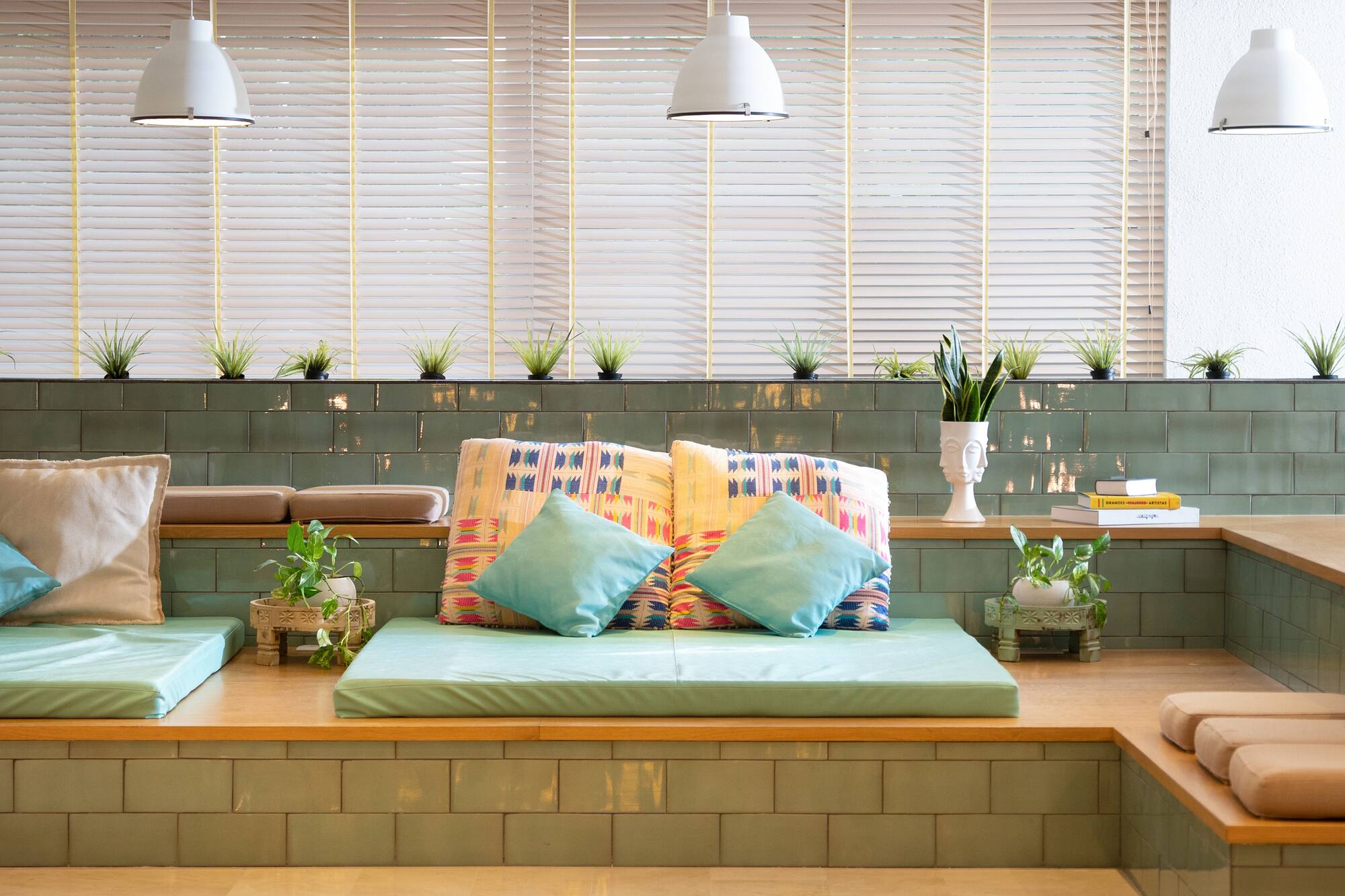 Lounge seating with green tiles, mint cushions, colorful pillows, and plants.