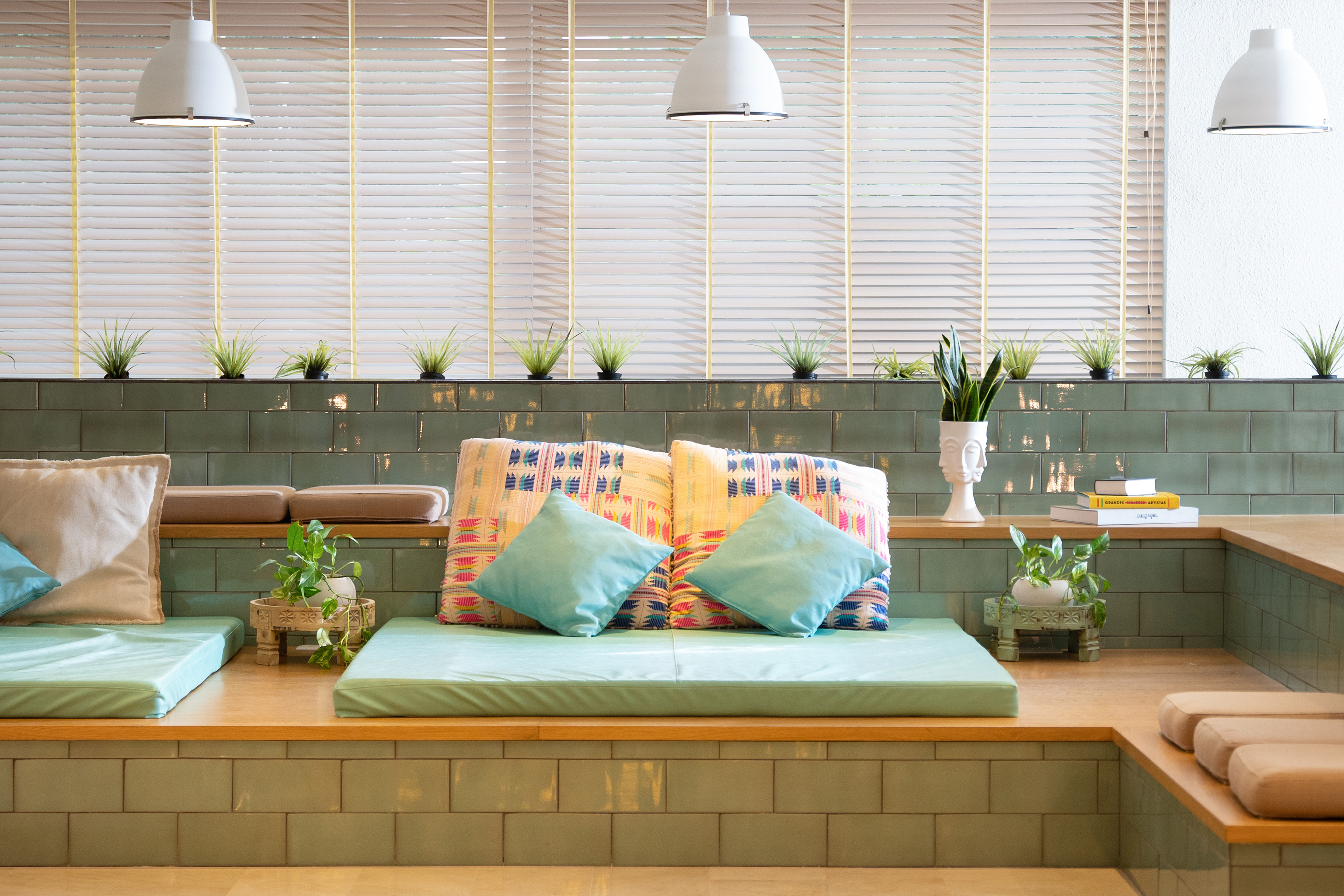 Lounge seating with green tiles, mint cushions, colorful pillows, and plants.