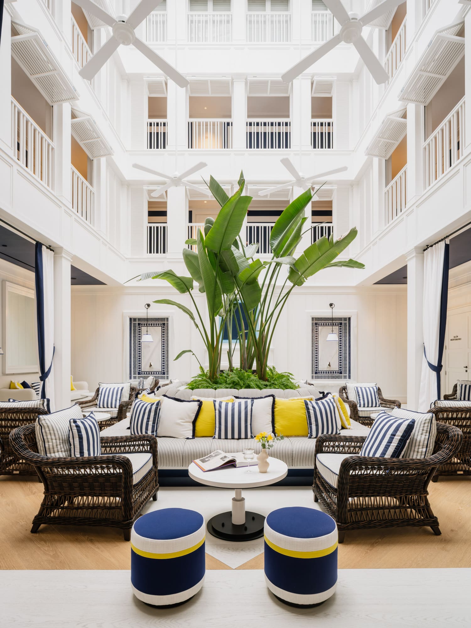 Nautical hotel lobby with wicker seating, striped cushions, and tropical plants.