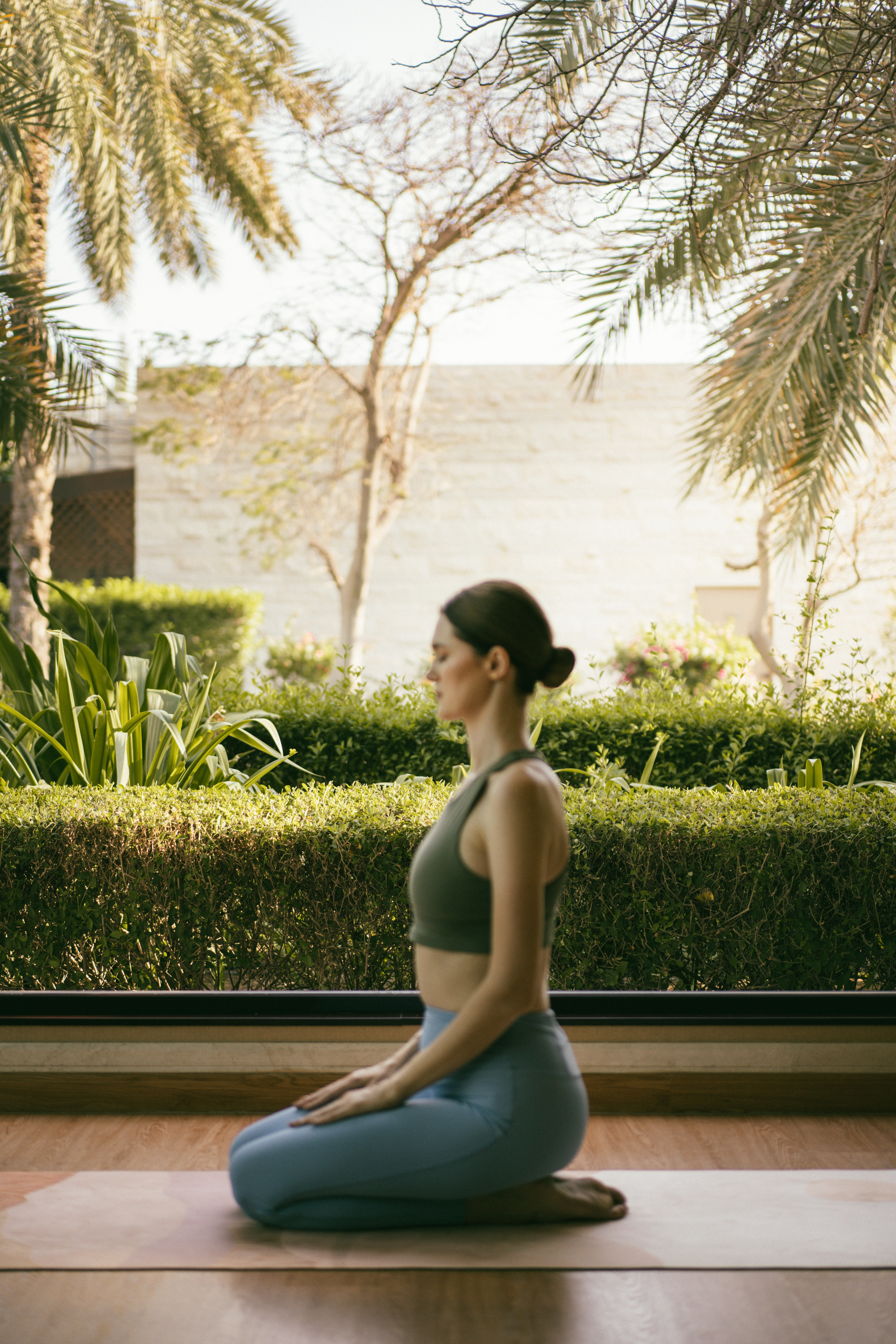 Woman meditating in yoga pose on mat outdoors with palm trees.