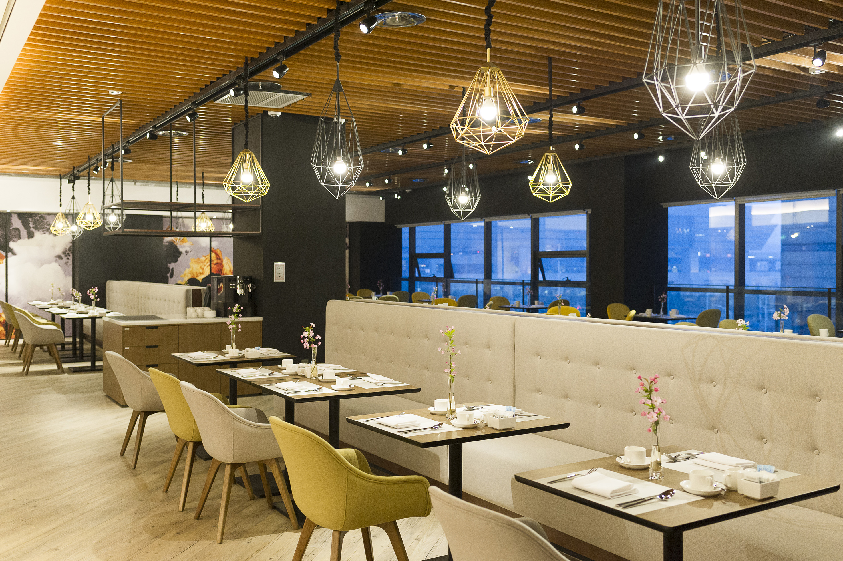 Modern dining interior with geometric lights, tables, and cozy booth seating.