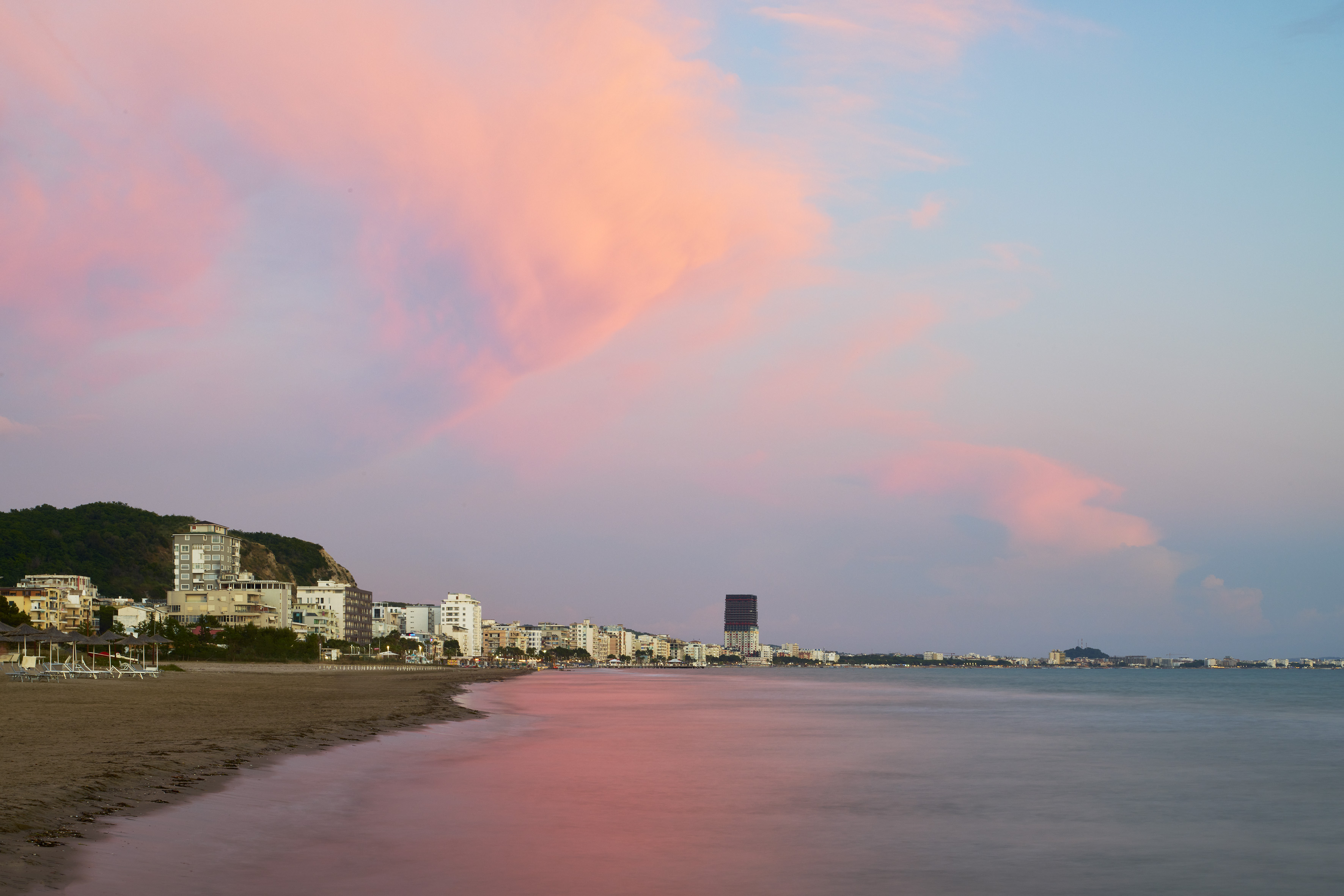 Pink sunset over coastal city beach skyline with tranquil sea reflections.