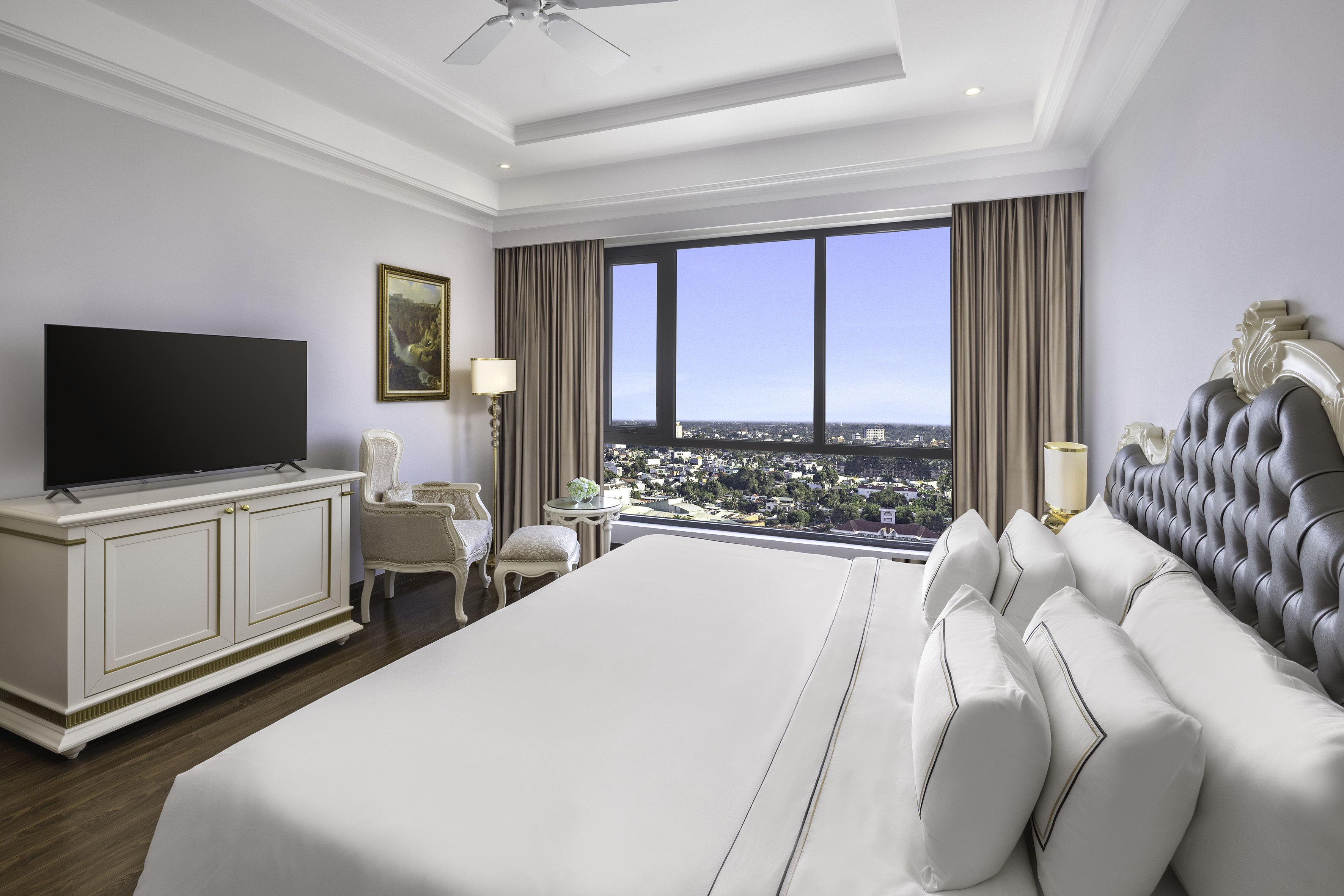 Luxury hotel bedroom with city view, elegant bed, and TV.