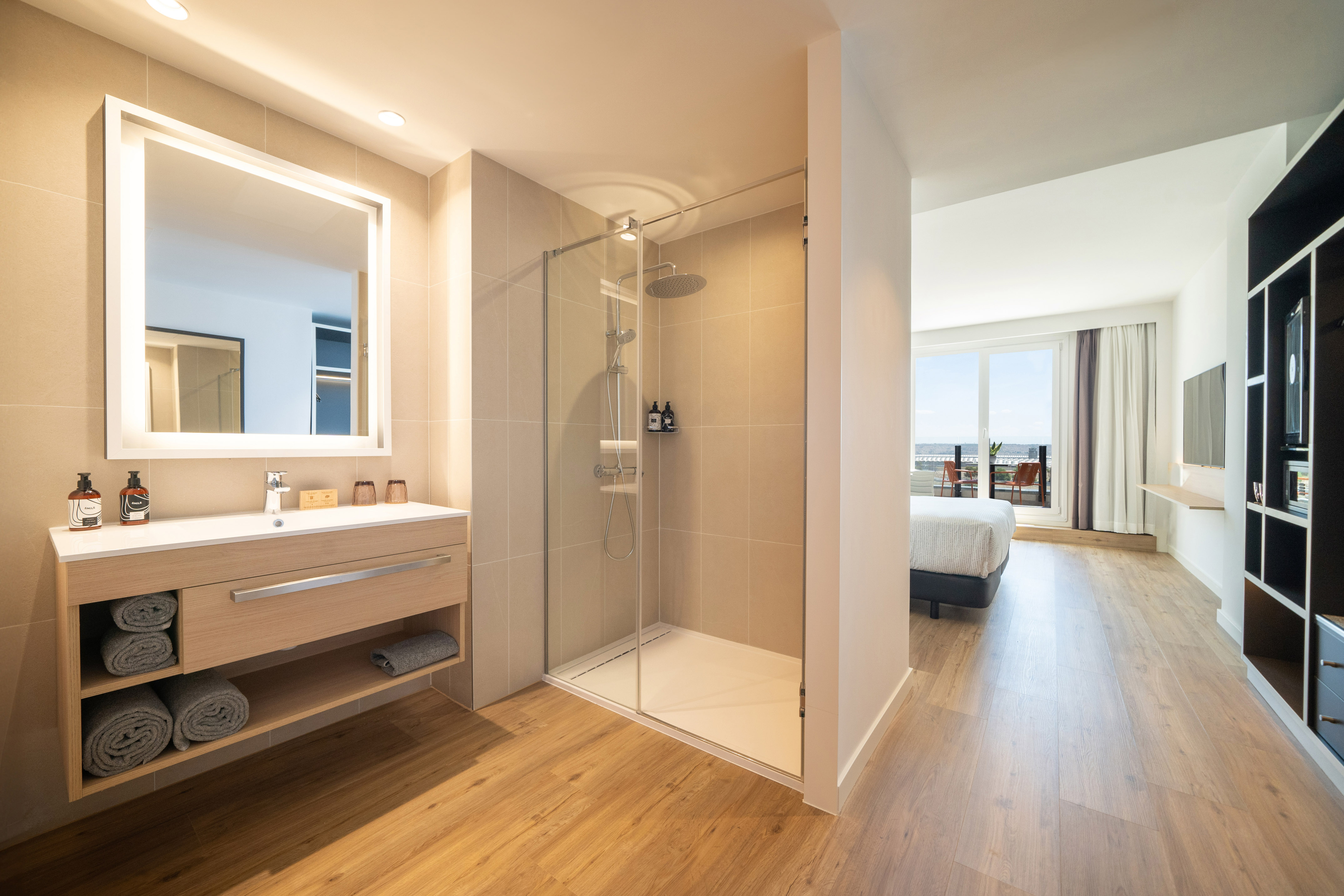 Modern hotel suite bathroom, walk-in shower, vanity, and ocean view bedroom.