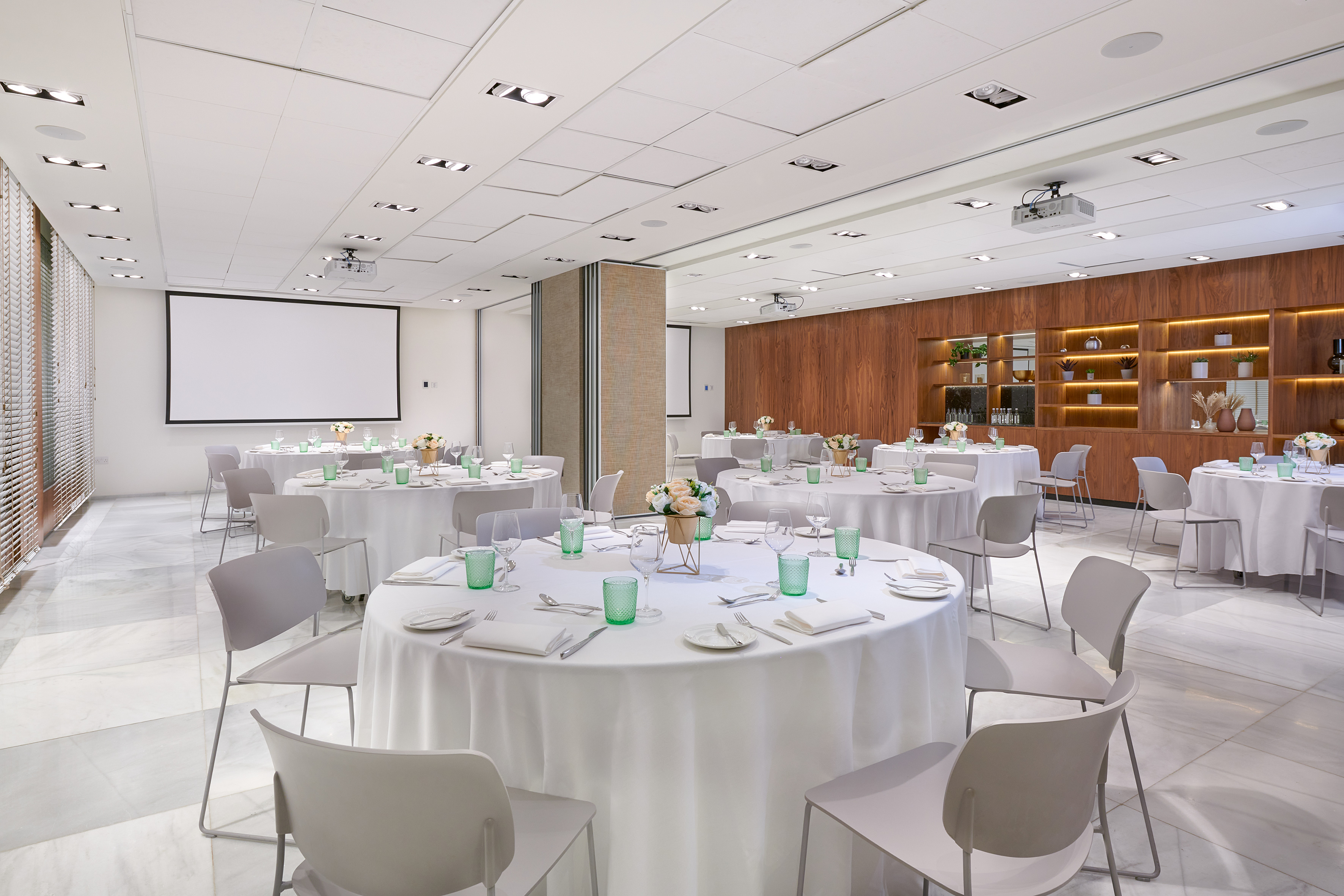 Modern event space with set dining tables, projector screen, and wood shelves.