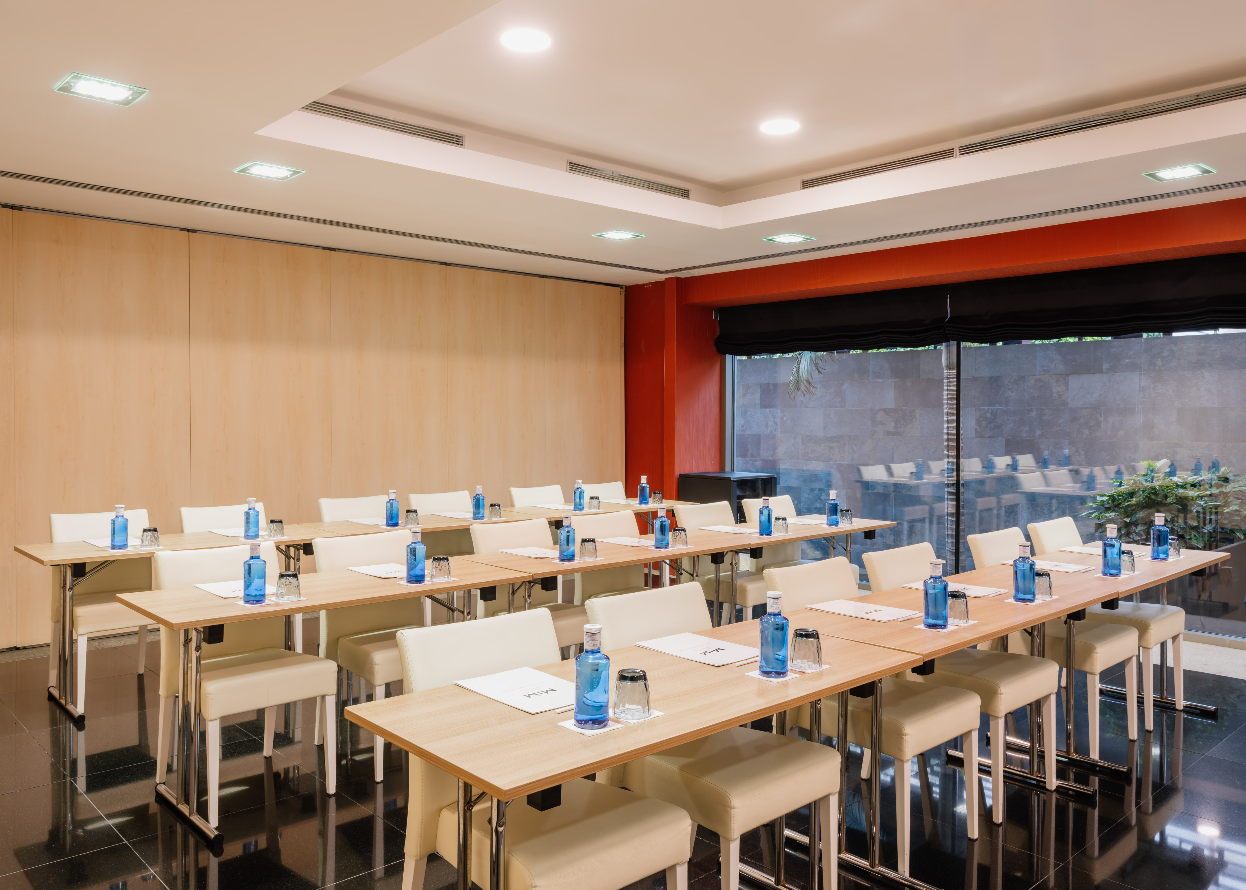 Classroom style meeting room with wood tables, beige chairs, and individual water bottles.