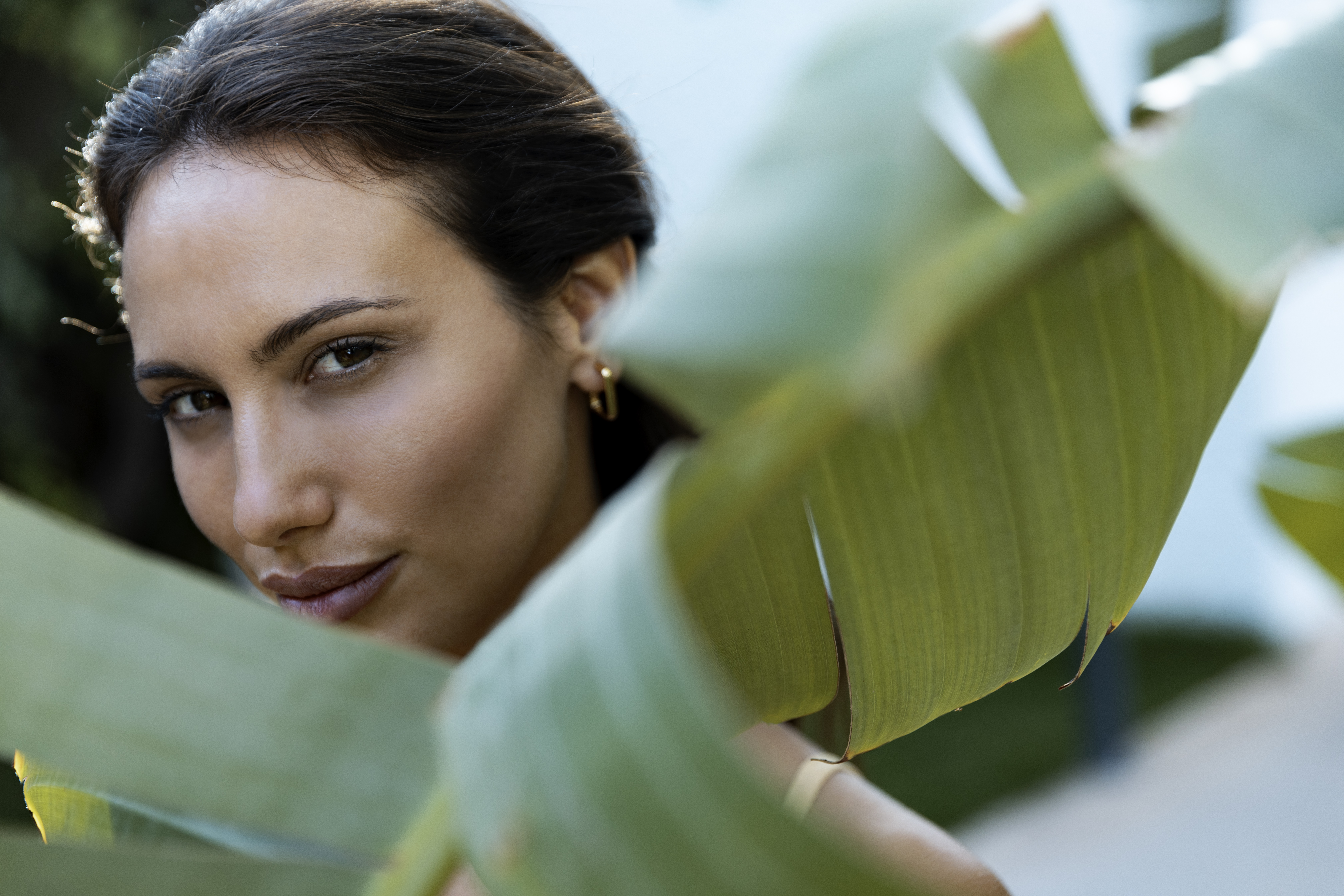 Woman's face framed by large green tropical leaves, looking at viewer.
