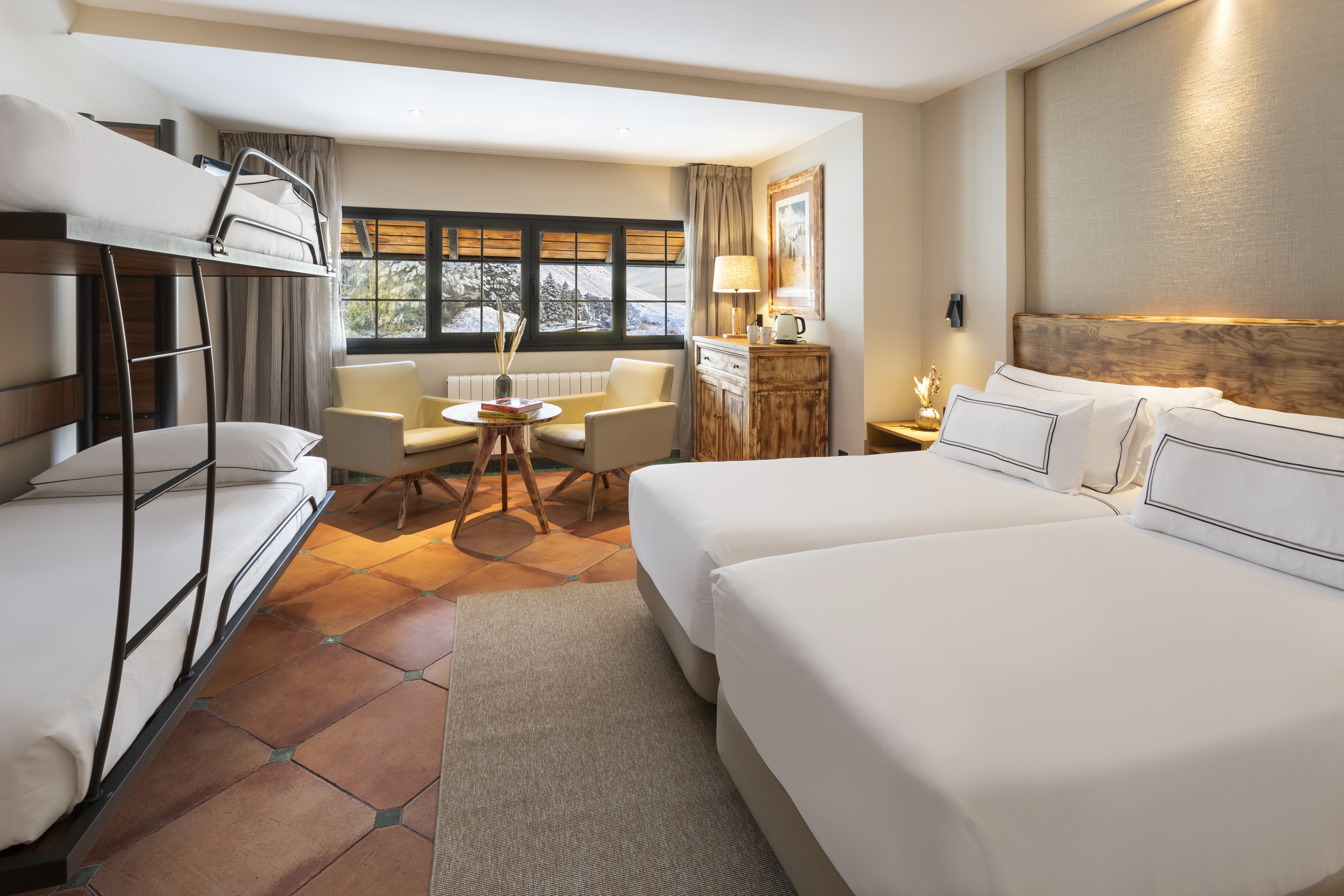 Cozy family hotel room with bunk bed, twin beds, and snowy mountain view.