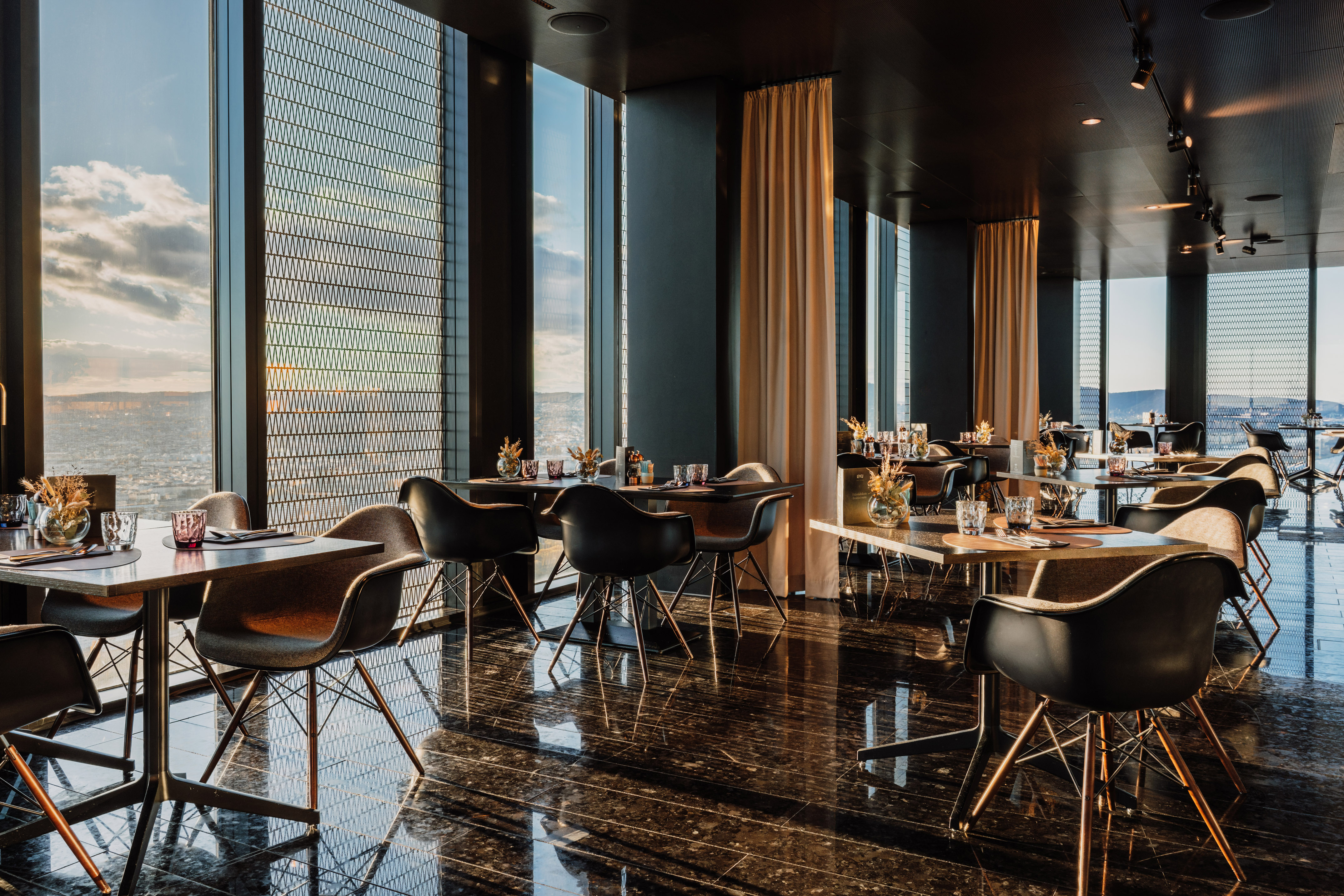 Elegant restaurant with panoramic city views, modern chairs, and glossy dark floor.