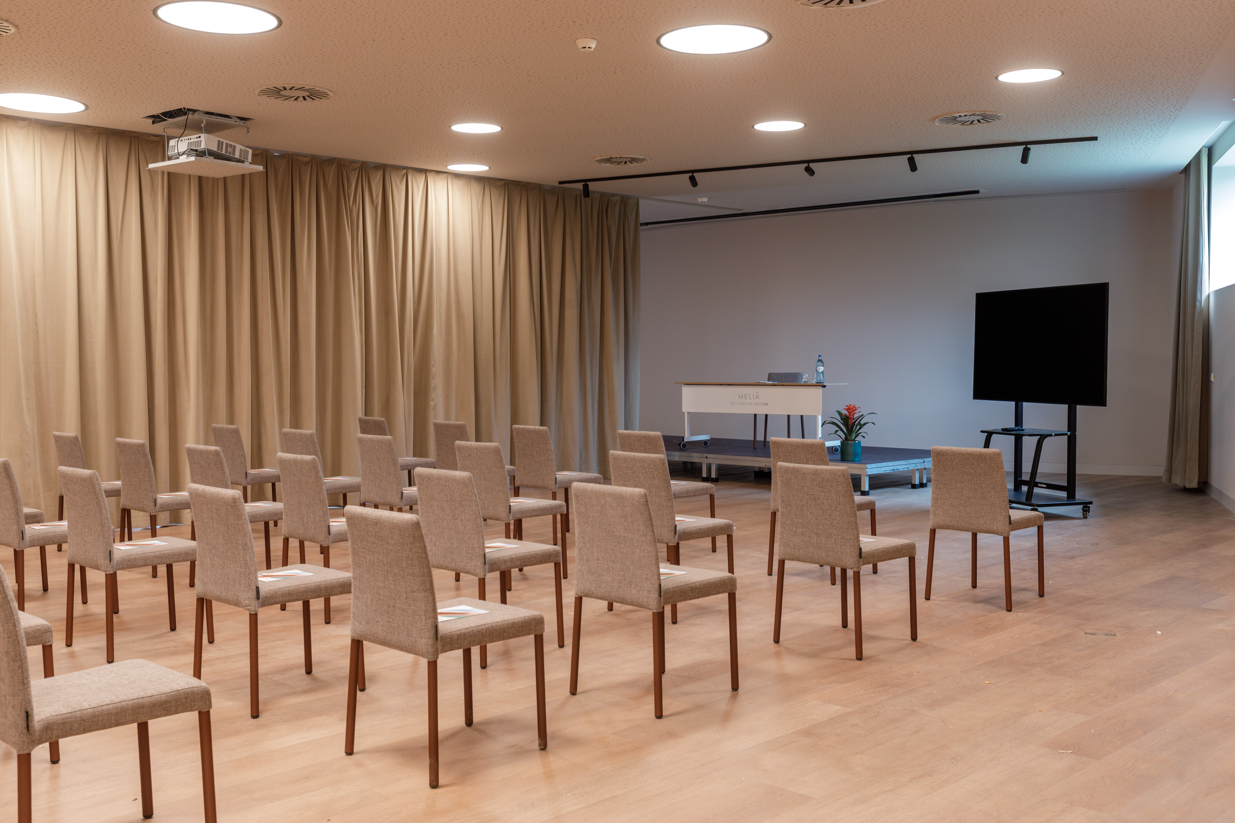 Modern meeting room with chairs, projector, lectern, and large screen.
