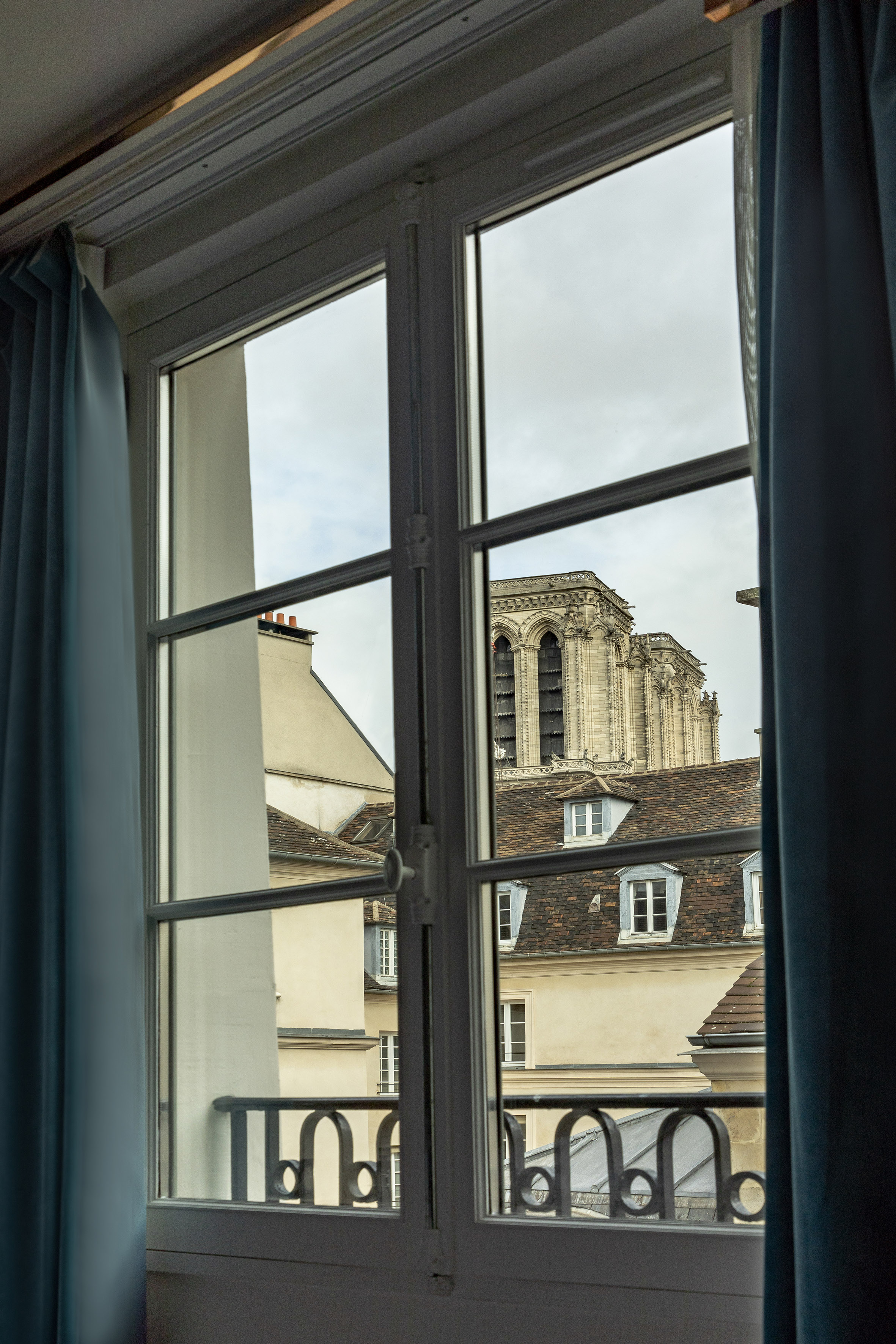 Parisian window overlooking Notre Dame Cathedral and traditional rooftops.