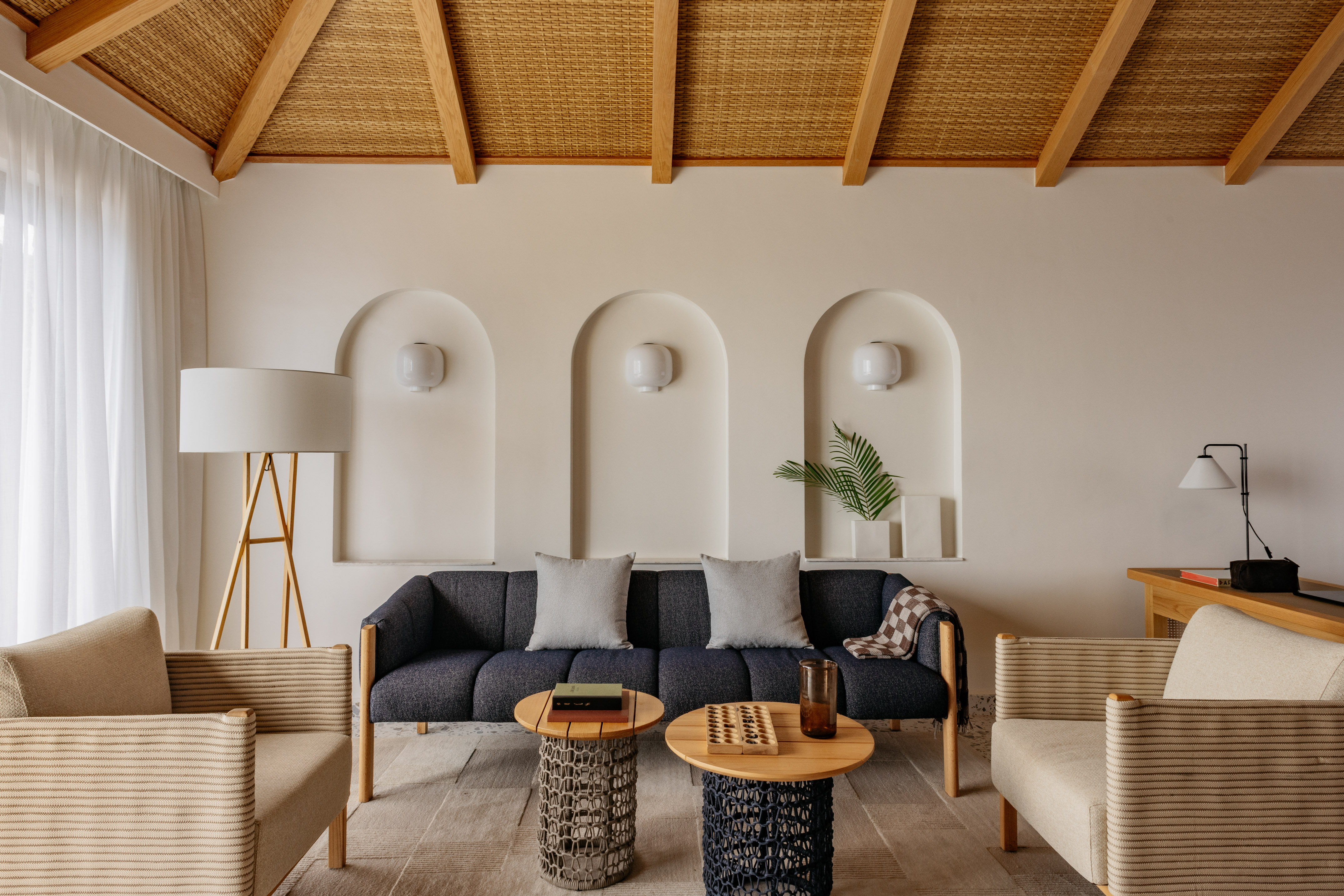 Cozy living room with dark sofa, armchairs, rattan ceiling, and arched walls.
