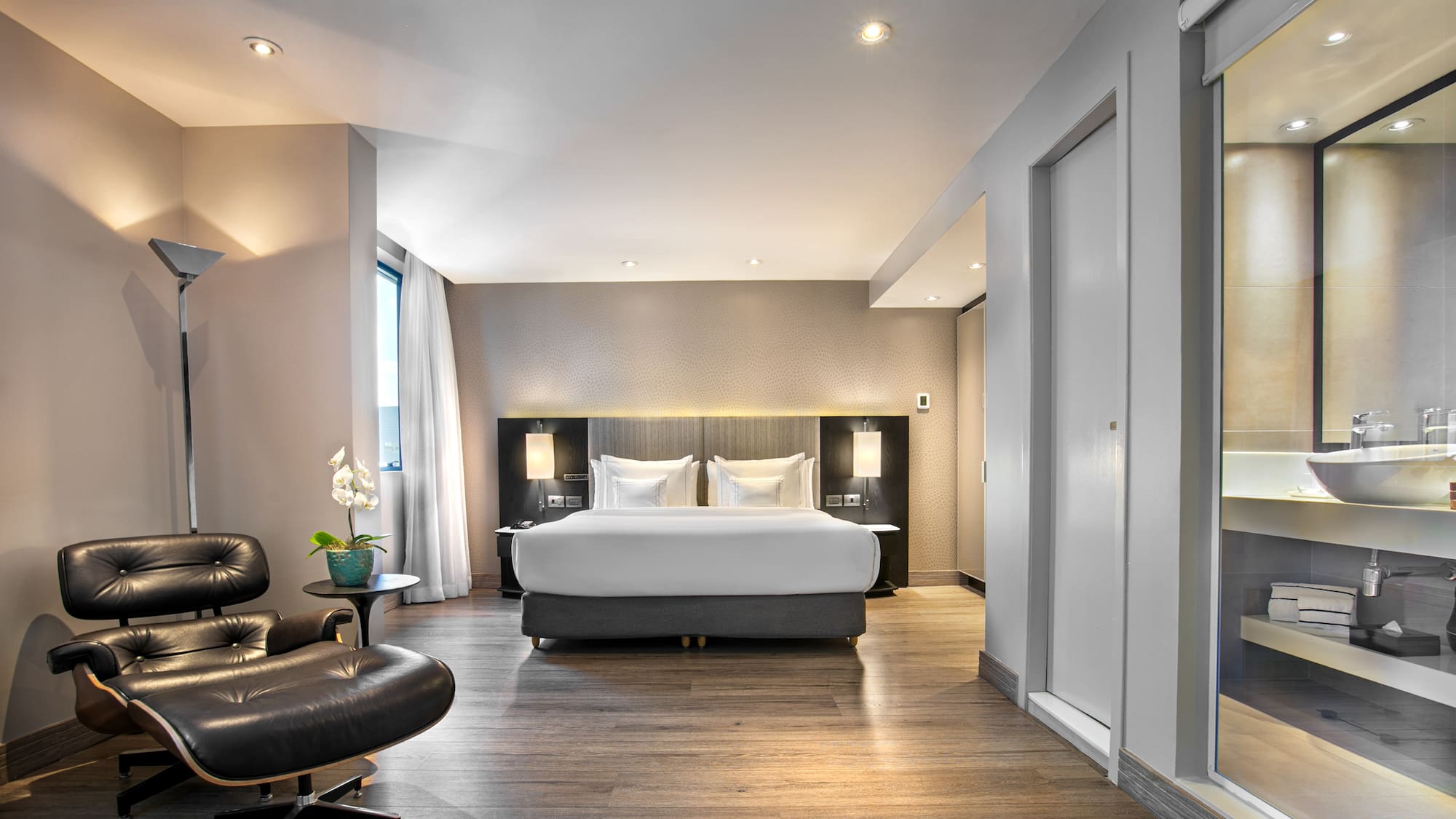 Luxury hotel bedroom suite with modern bed, Eames lounge chair, and wood floor.
