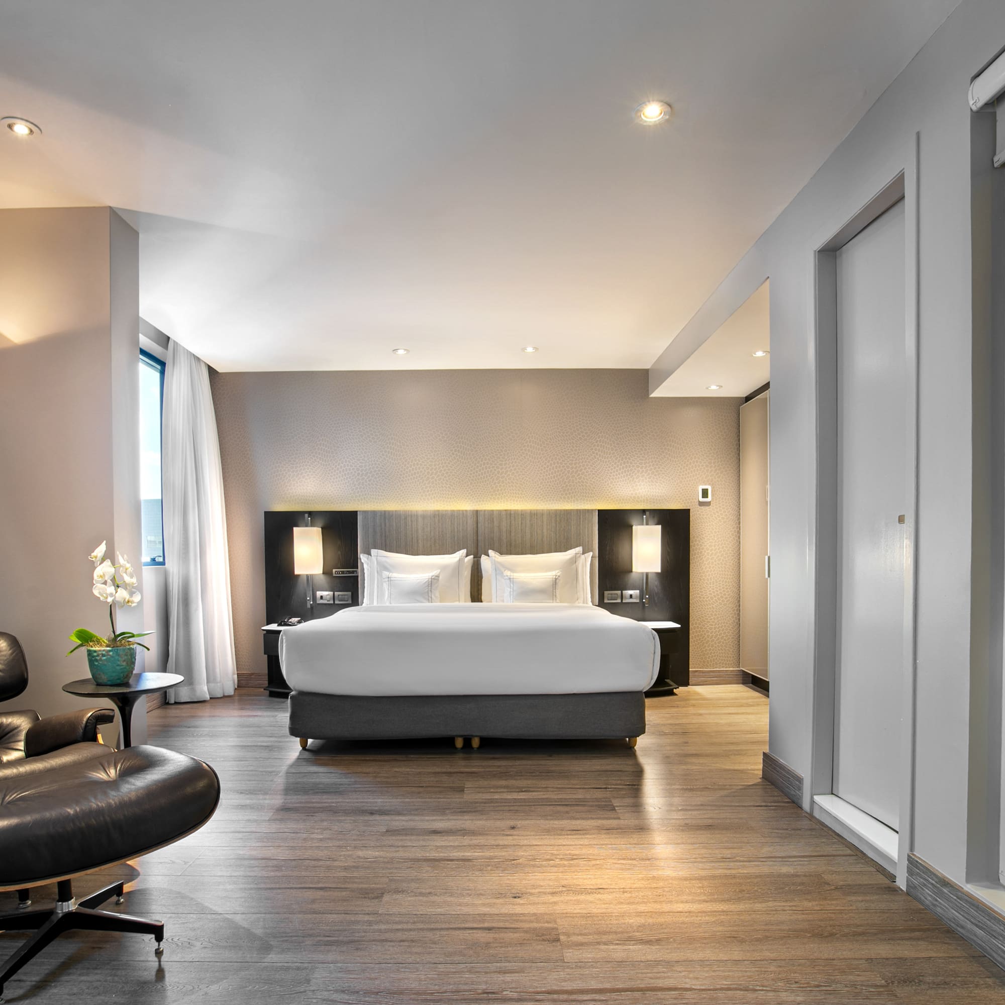 Luxury hotel bedroom suite with modern bed, Eames lounge chair, and wood floor.