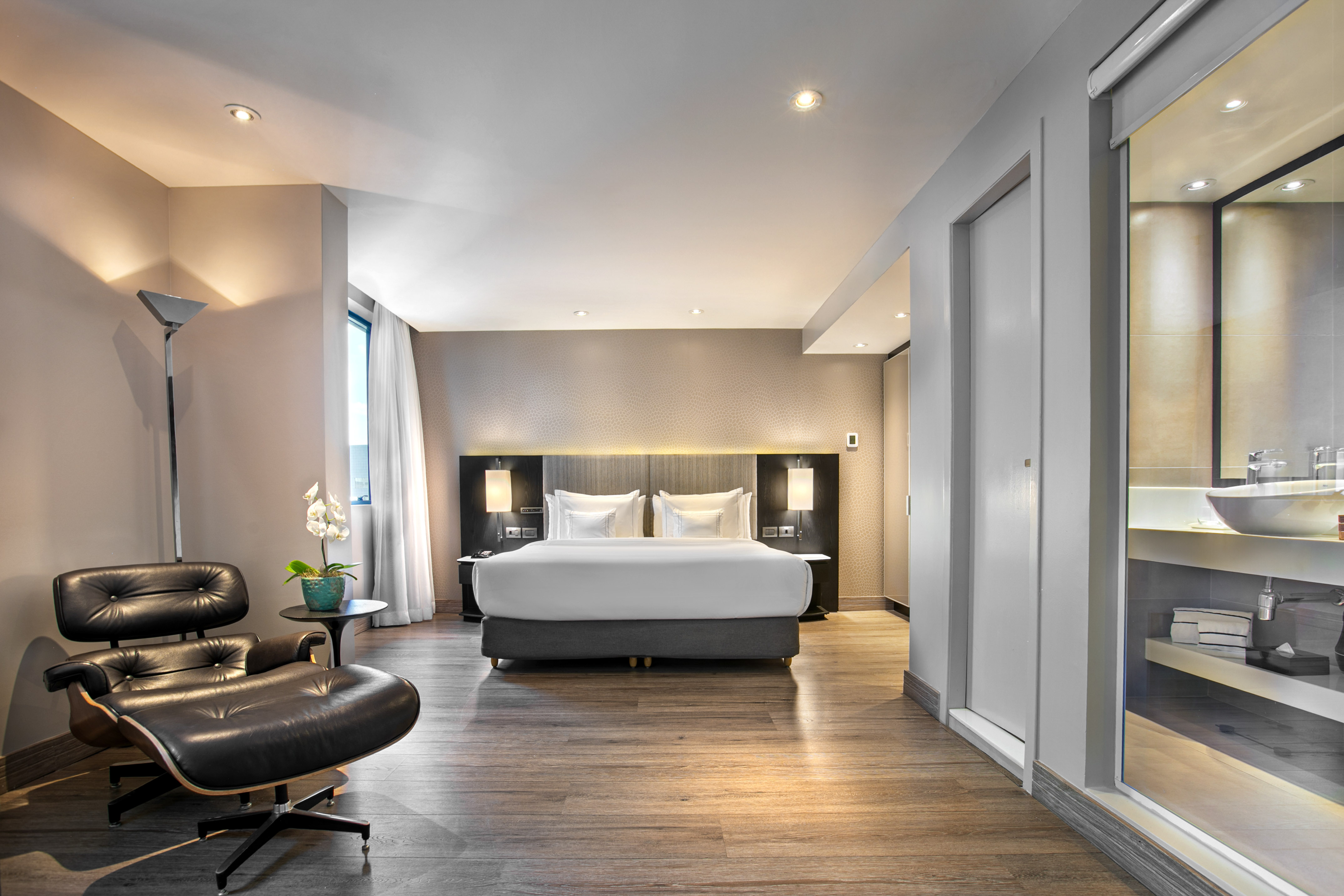 Luxury hotel bedroom suite with modern bed, Eames lounge chair, and wood floor.