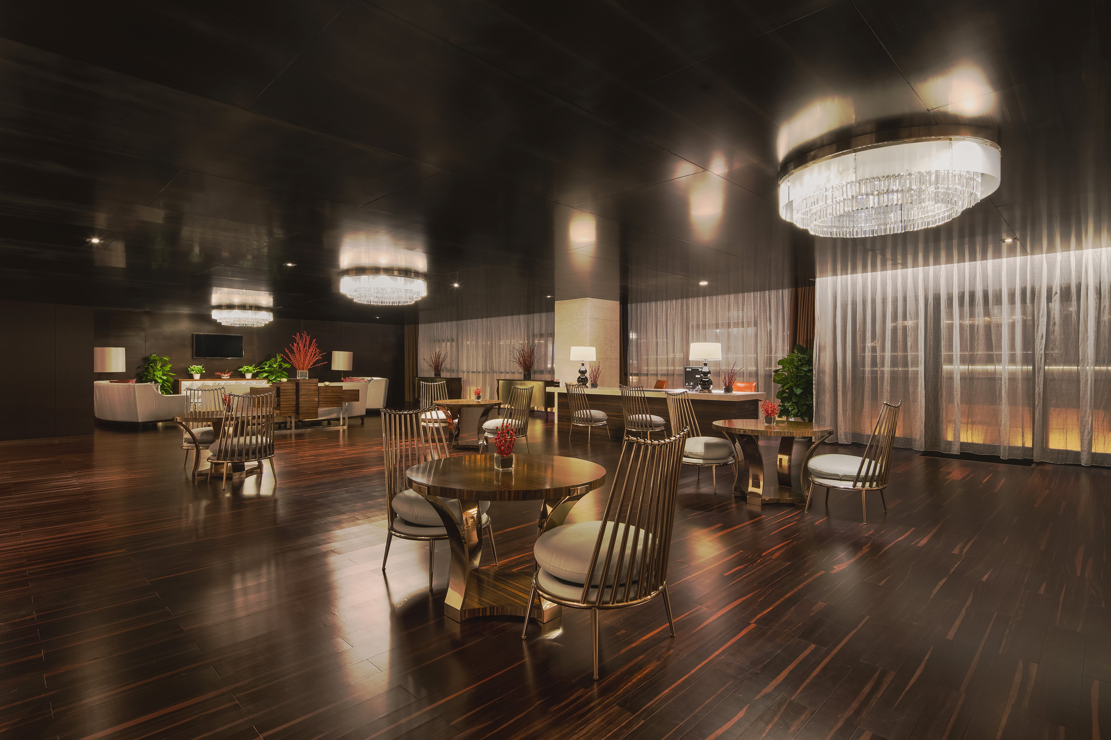 Elegant hotel lobby lounge with dark wood, gold chairs, and chandeliers.