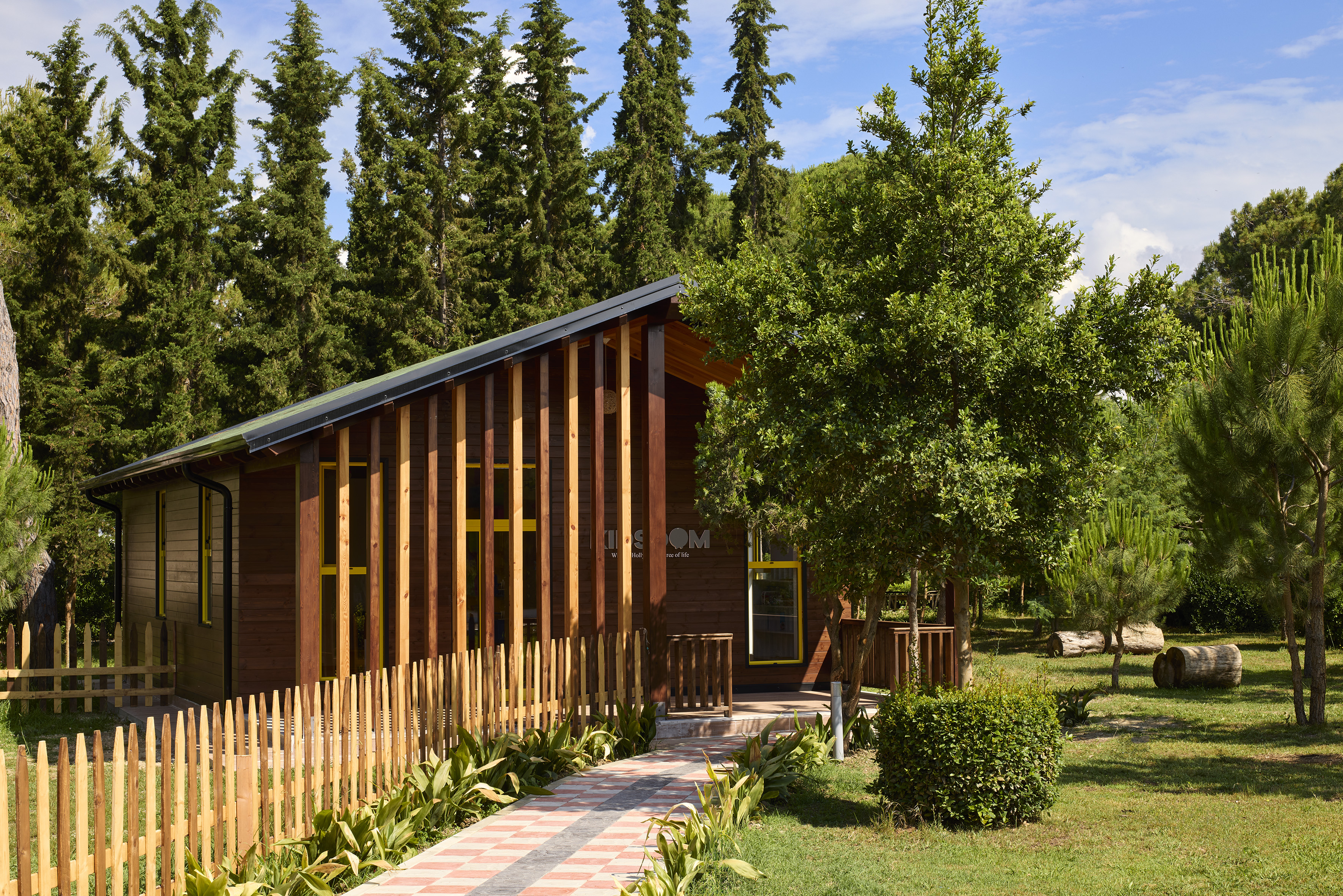 Wooden lodge cabin with a picket fence among tall pine trees.