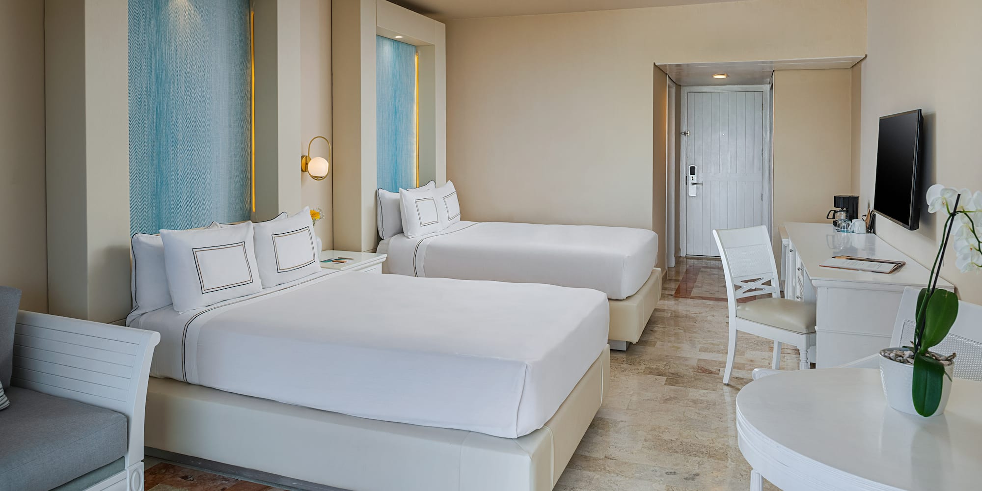 Modern hotel room with two beds, blue accents, white furniture, and tiled floor.