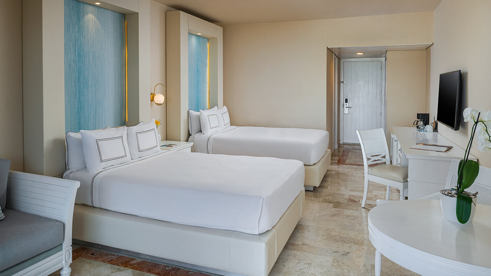 Modern hotel room with two beds, blue accents, white furniture, and tiled floor.
