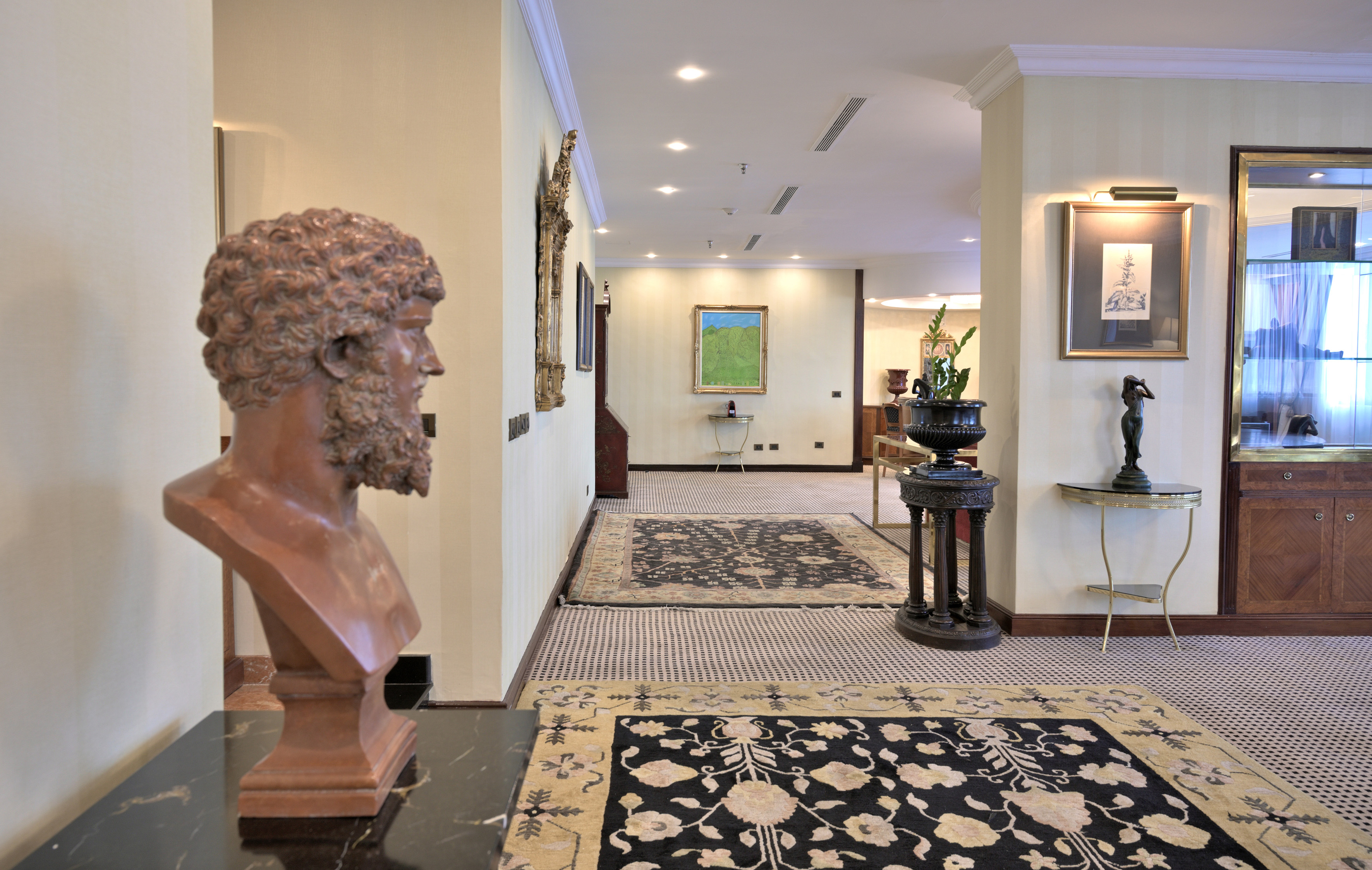 Classical bust in luxurious hotel lobby with art and patterned carpets.
