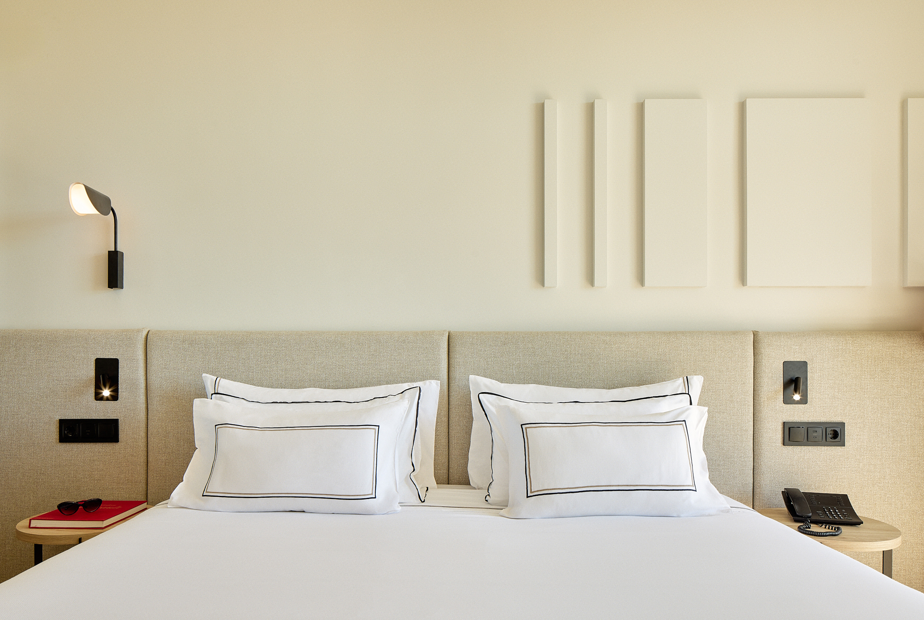 Modern hotel bedroom with white bed, striped pillows, and neutral headboard.