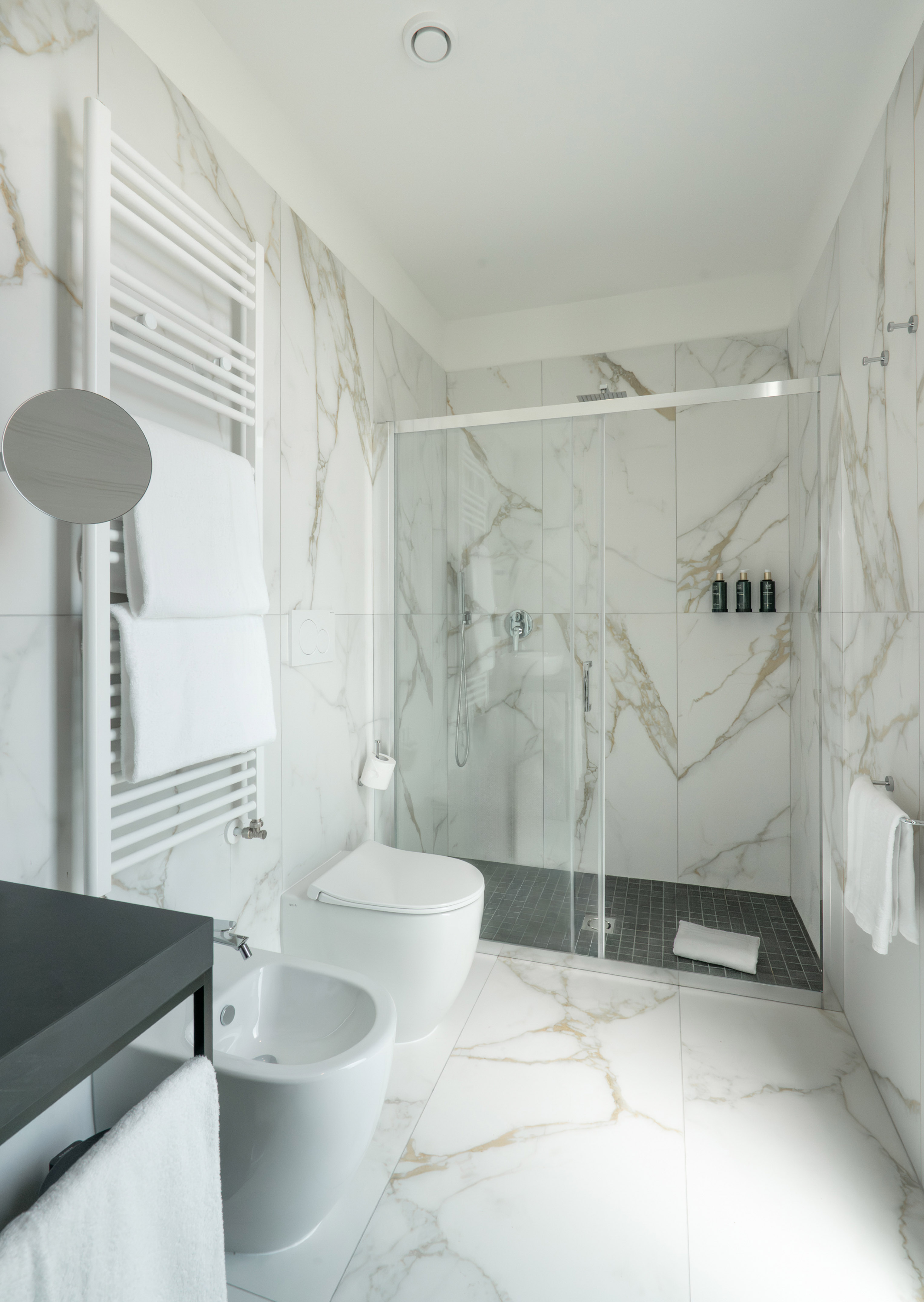 Modern bathroom with white and gold marble, shower, toilet, bidet, and towel warmer.