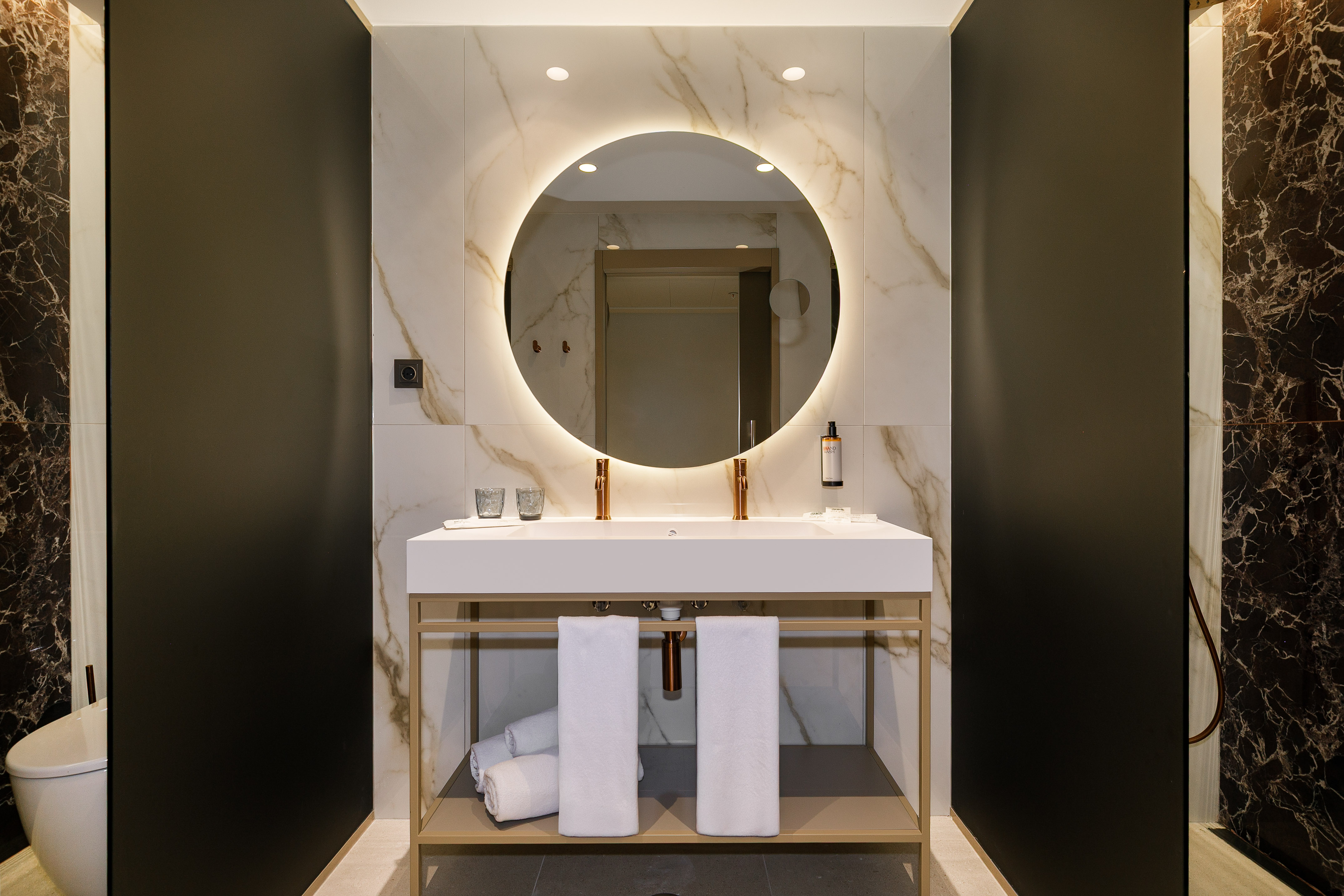 Sleek double vanity bathroom with glowing round mirror and marble.
