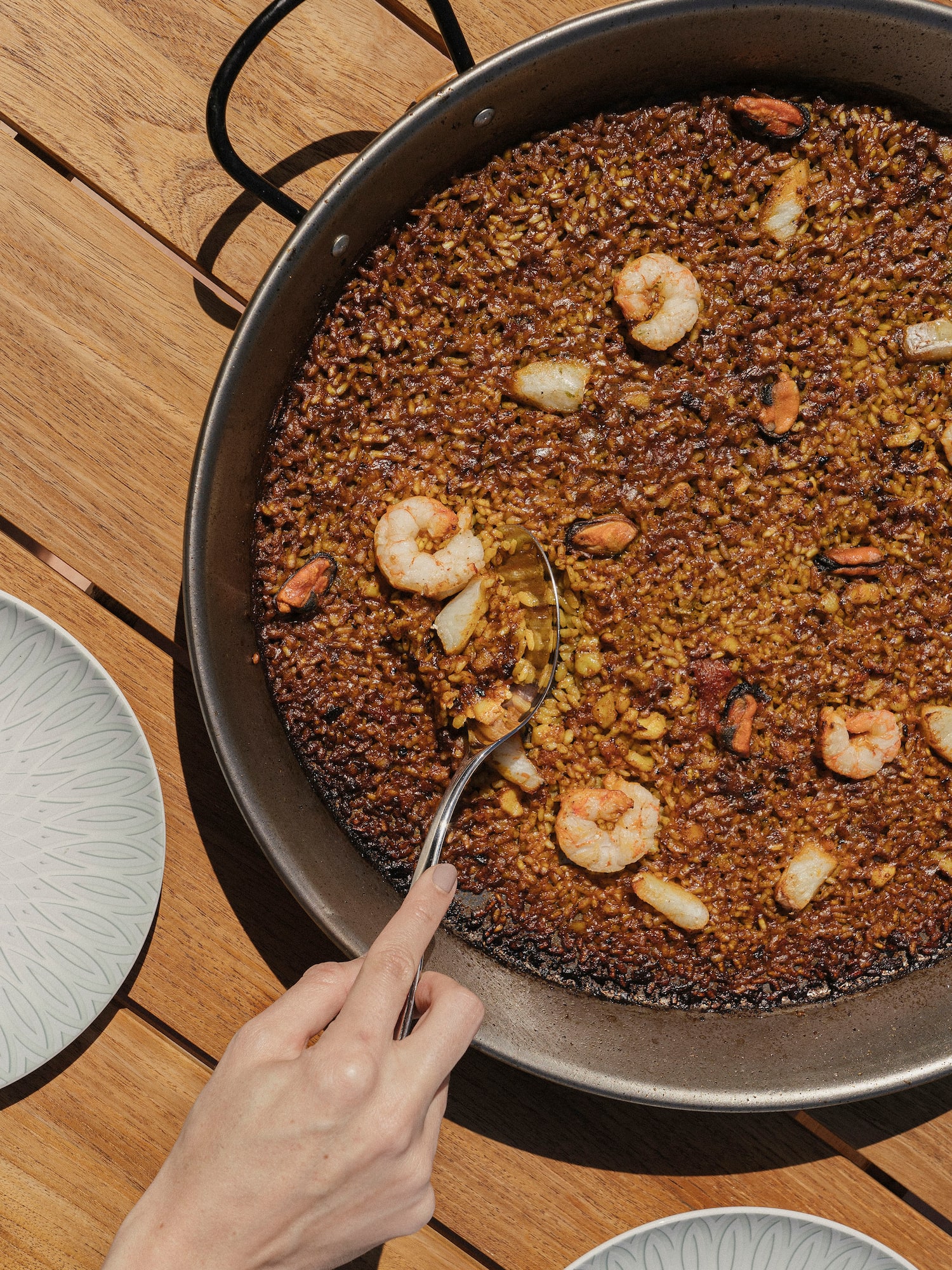 a hand holding a spoon over a pan of rice with shrimp