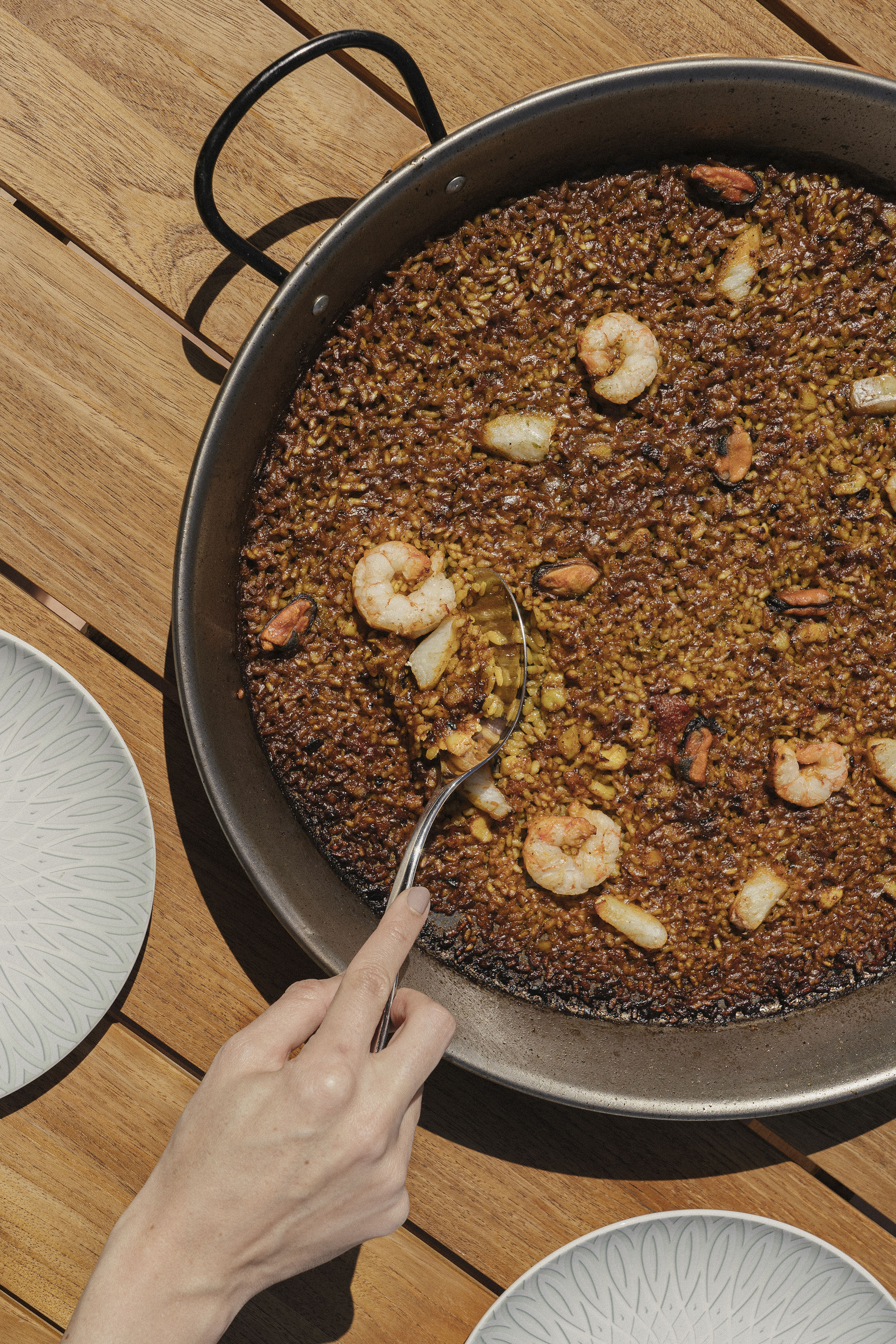 Seafood paella (arroz negro) with shrimp, mussels served from a pan on wood.