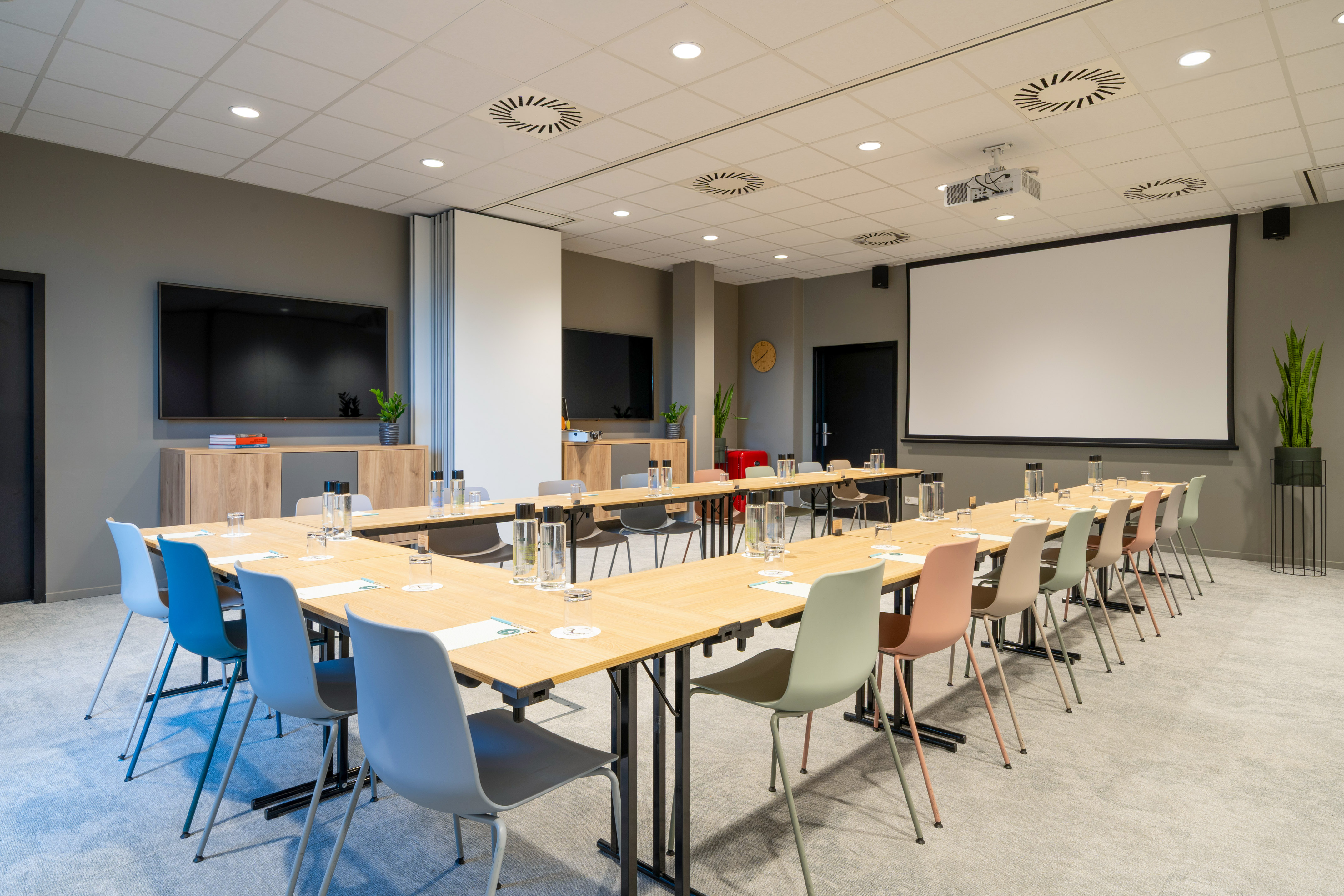 Modern meeting room with U-shaped table, projector screen, and TV.