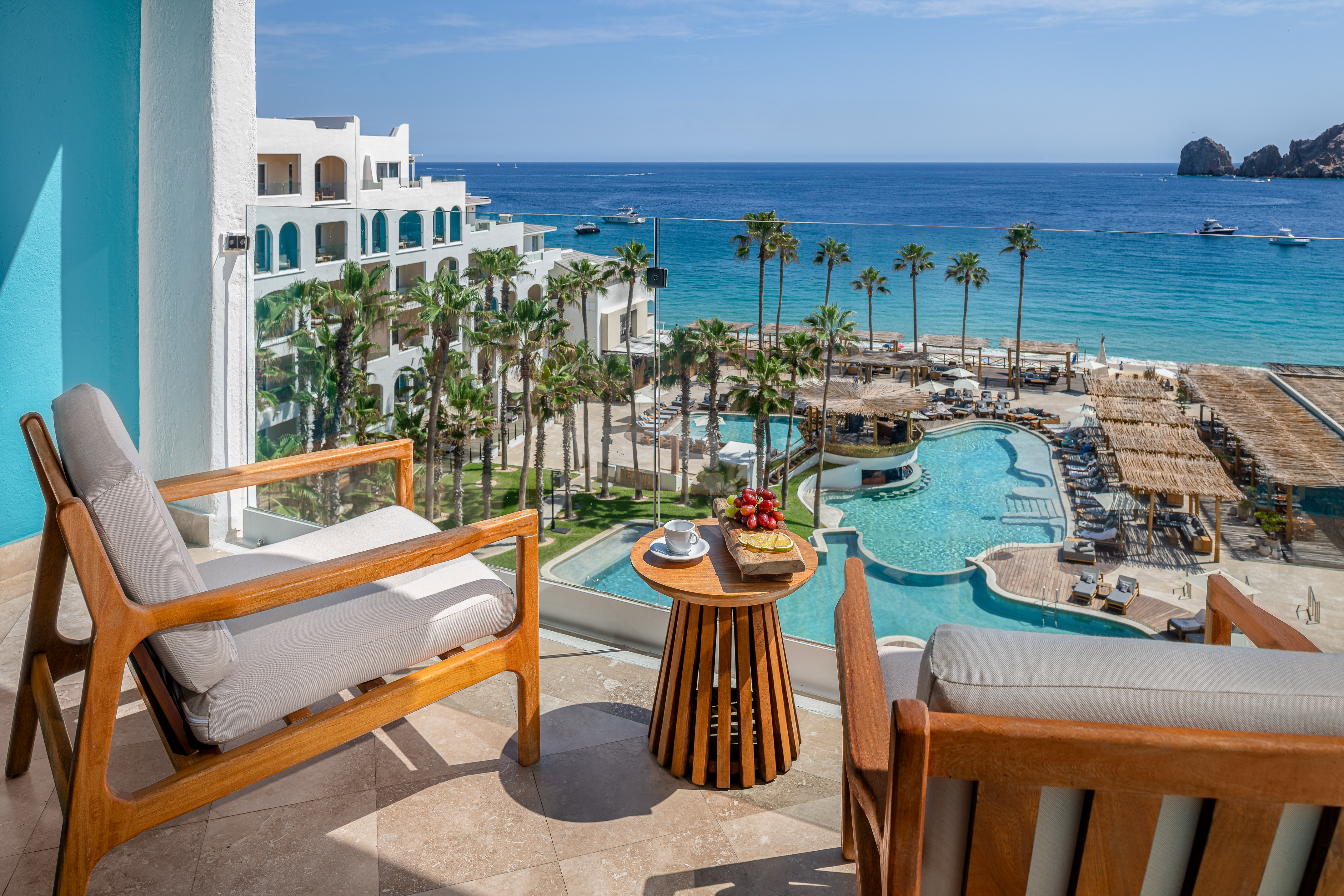 Hotel balcony with ocean view, beach, tropical pools, and palm trees.