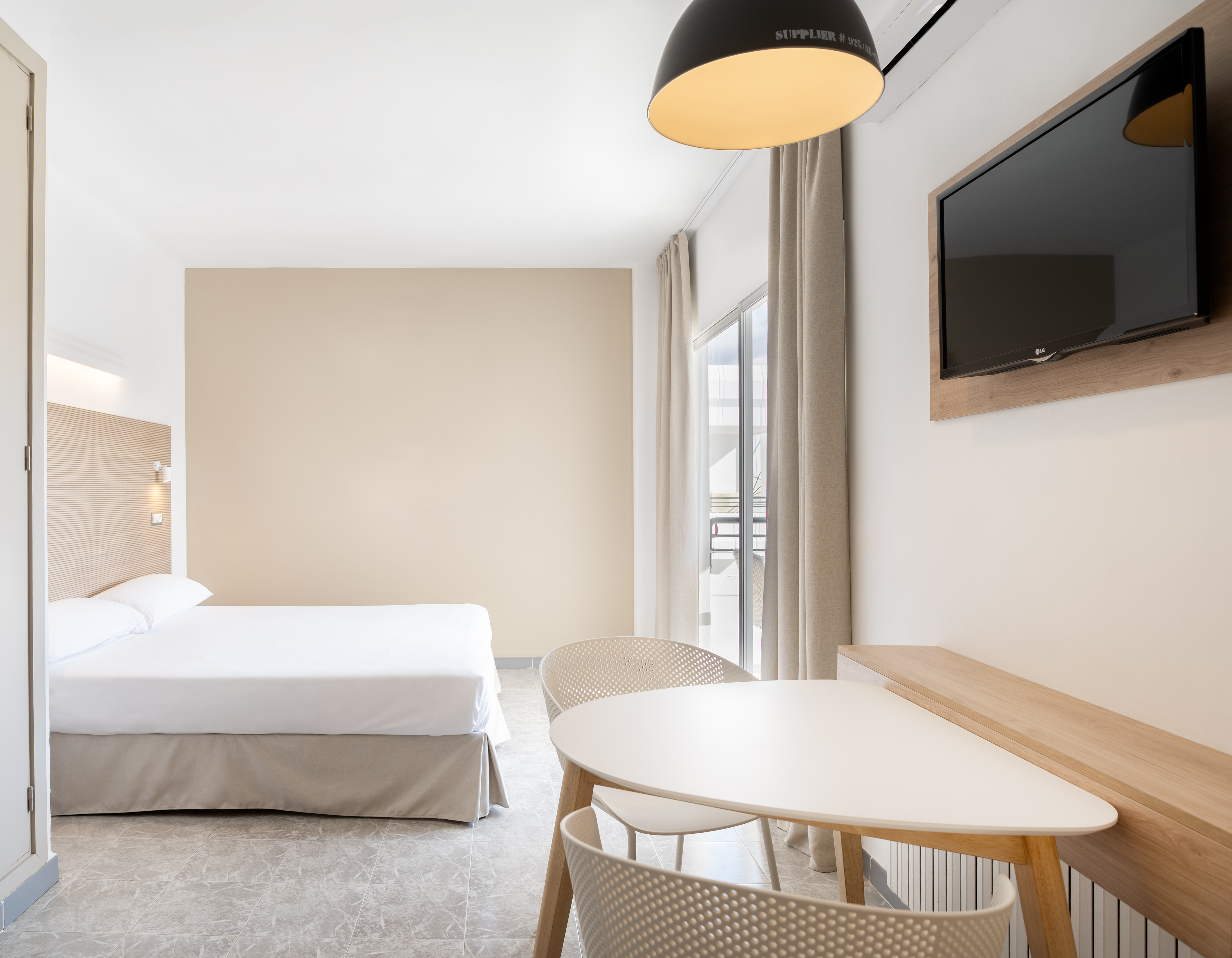 Bright hotel room interior with bed, dining, TV, and balcony.
